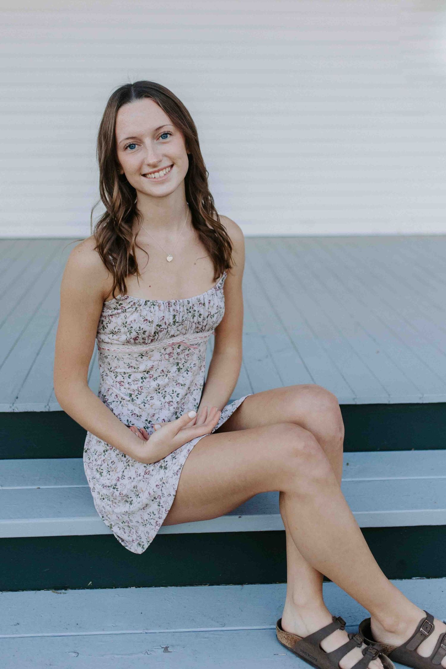 Casual portrait session on a porch wearing a floral summer dress and sandals.