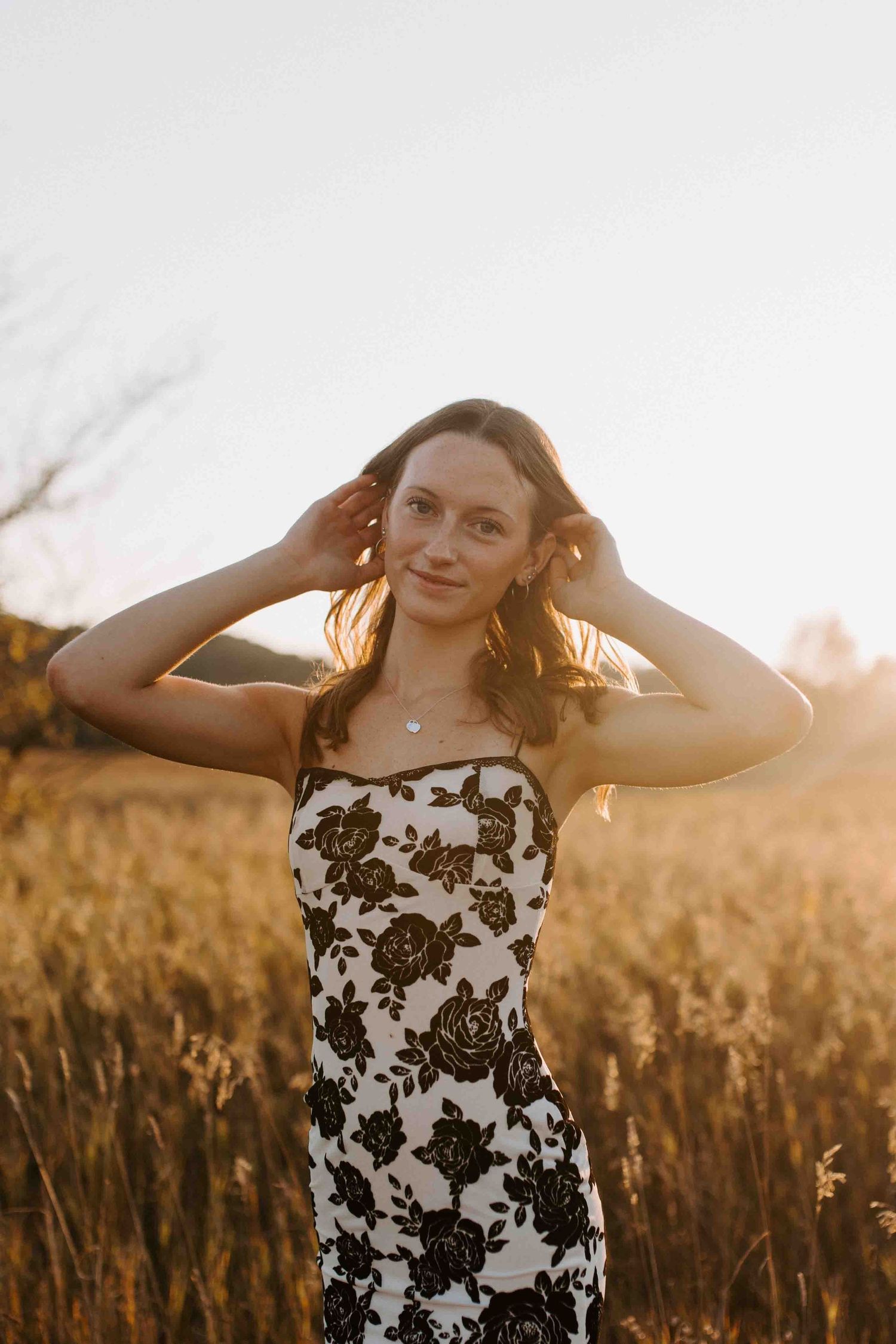 Sunlit portrait in a black and white floral dress against autumn fields.