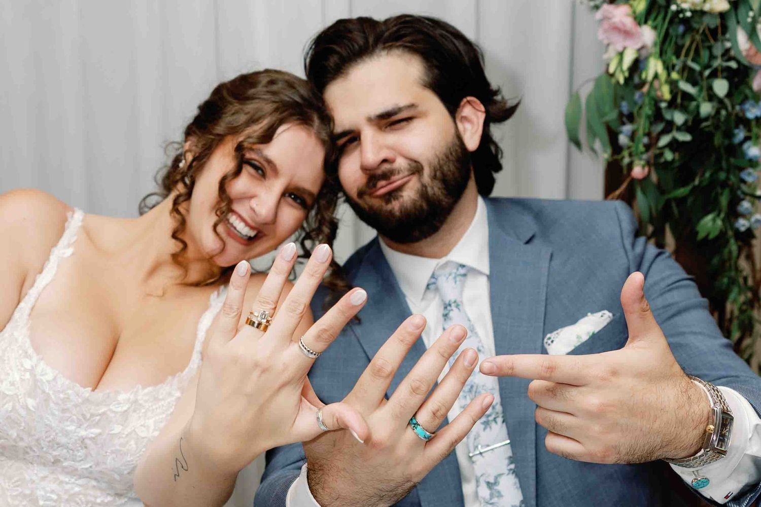 Wedding couple showing off rings and celebrating their marriage outdoors.