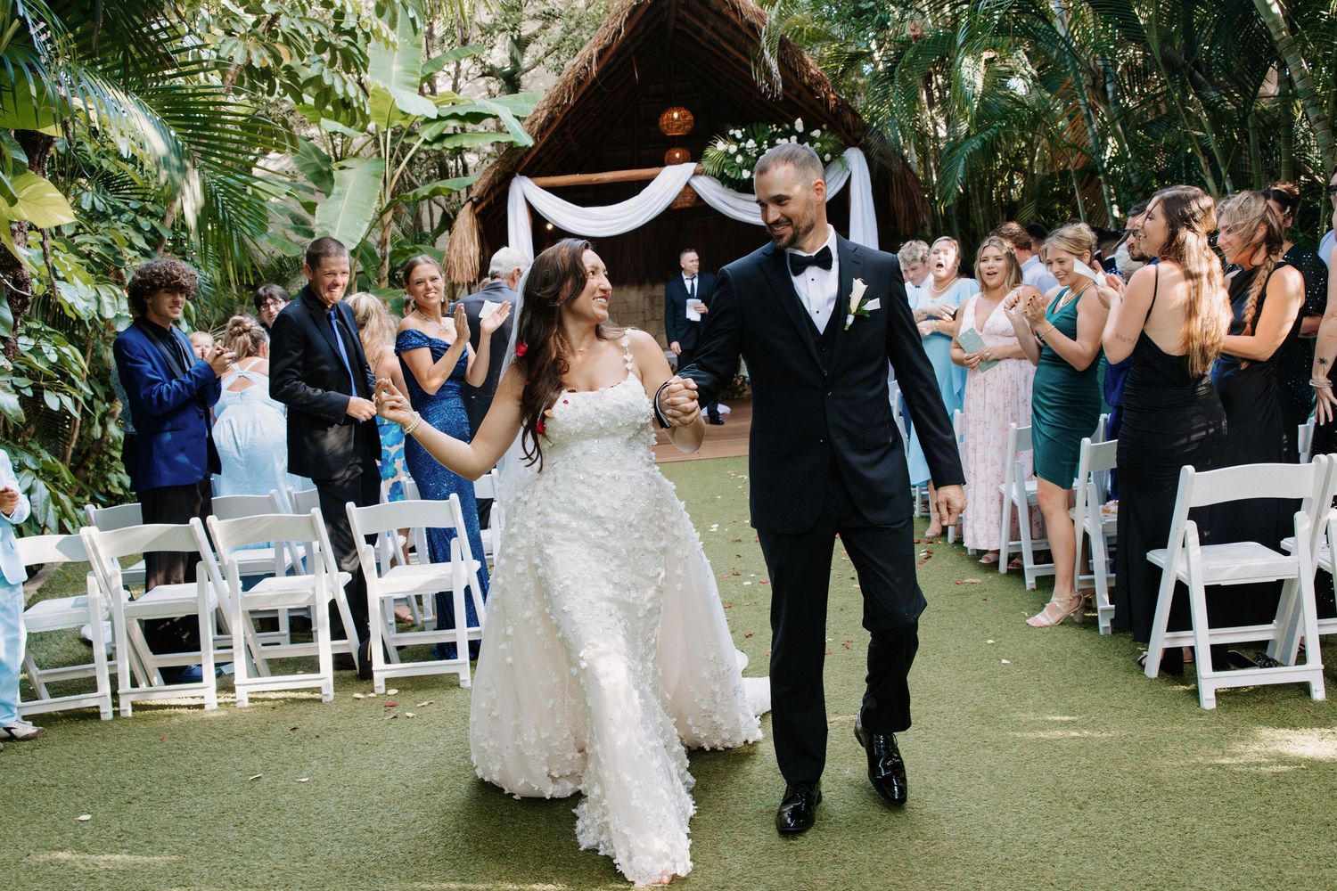 Outdoor wedding ceremony setup with white chairs and tropical greenery in a garden setting.
