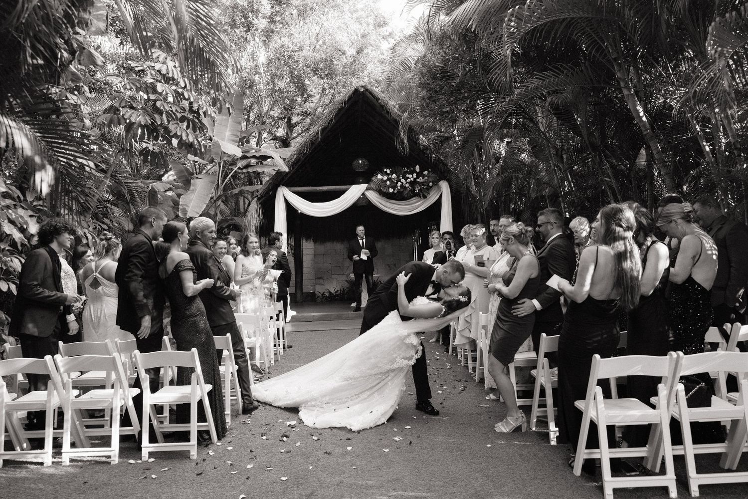 Black and white photo of an outdoor wedding ceremony with rows of chairs and guests.