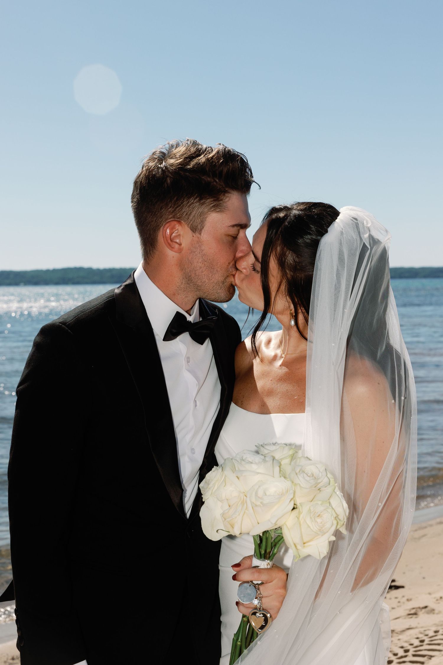 Romantic beach wedding portraits with white bouquet and flowing veil against ocean backdrop.