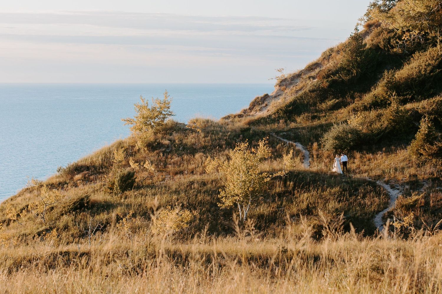Wedding couple walking along scenic coastal hillside during golden hour.