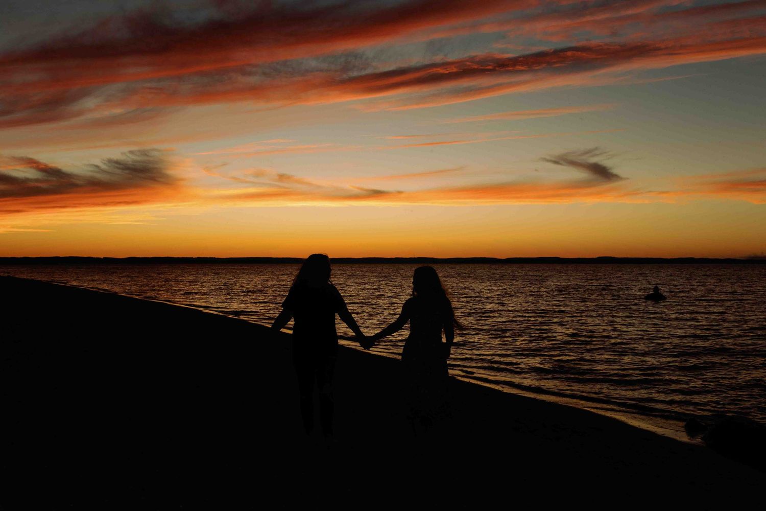 Silhouettes against a vivid orange sunset sky over tranquil ocean waters.