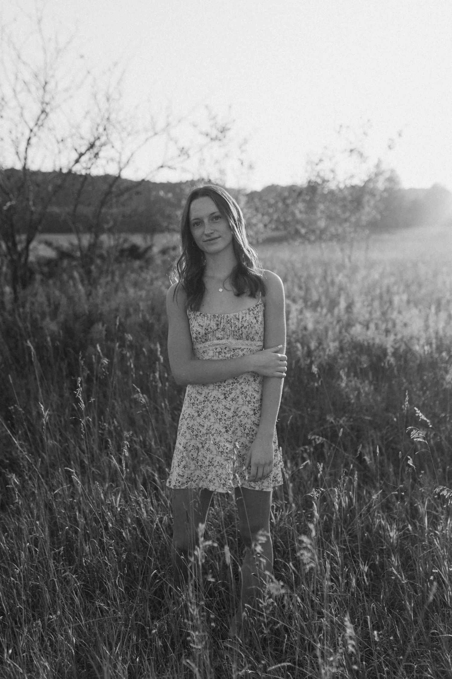 Black and white portrait in a field showing a floral sundress against wild grasses.