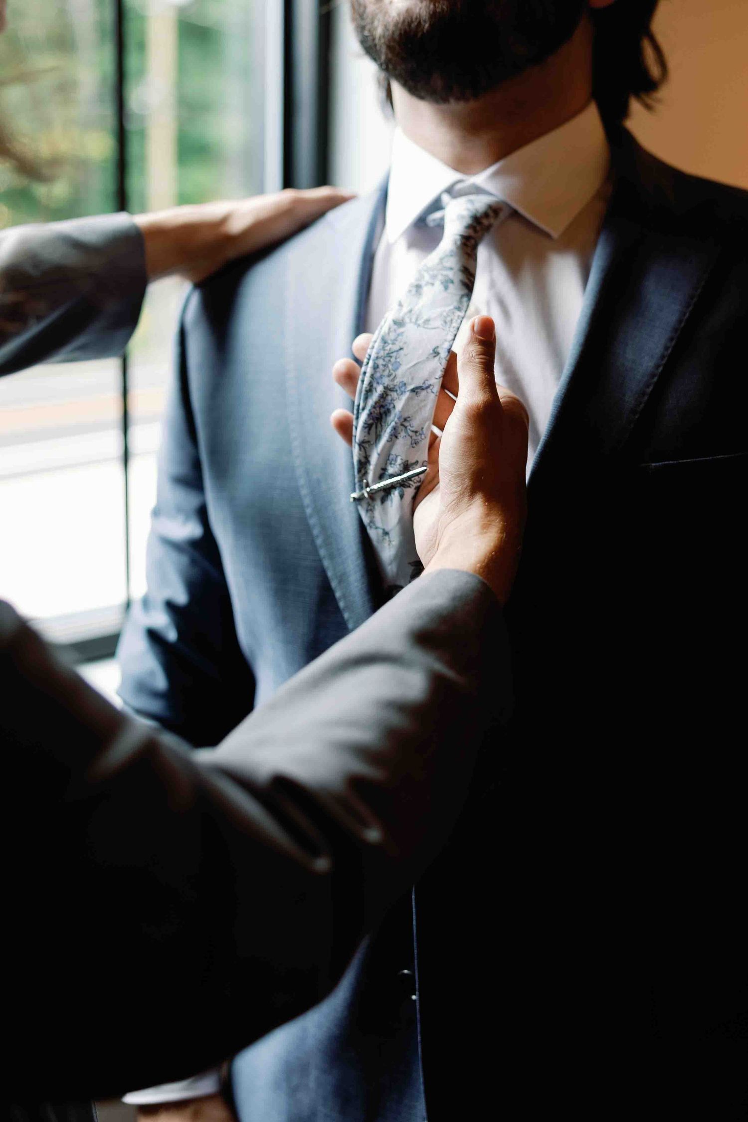 Close-up shot of someone adjusting a formal tie and suit collar.