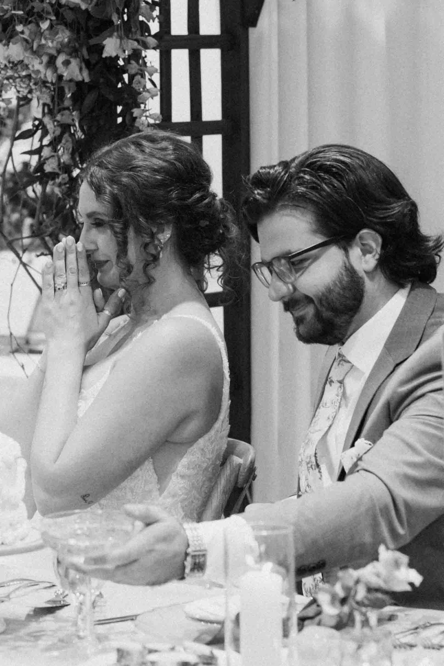 Black and white photo of wedding guests seated at reception tables during emotional moments.