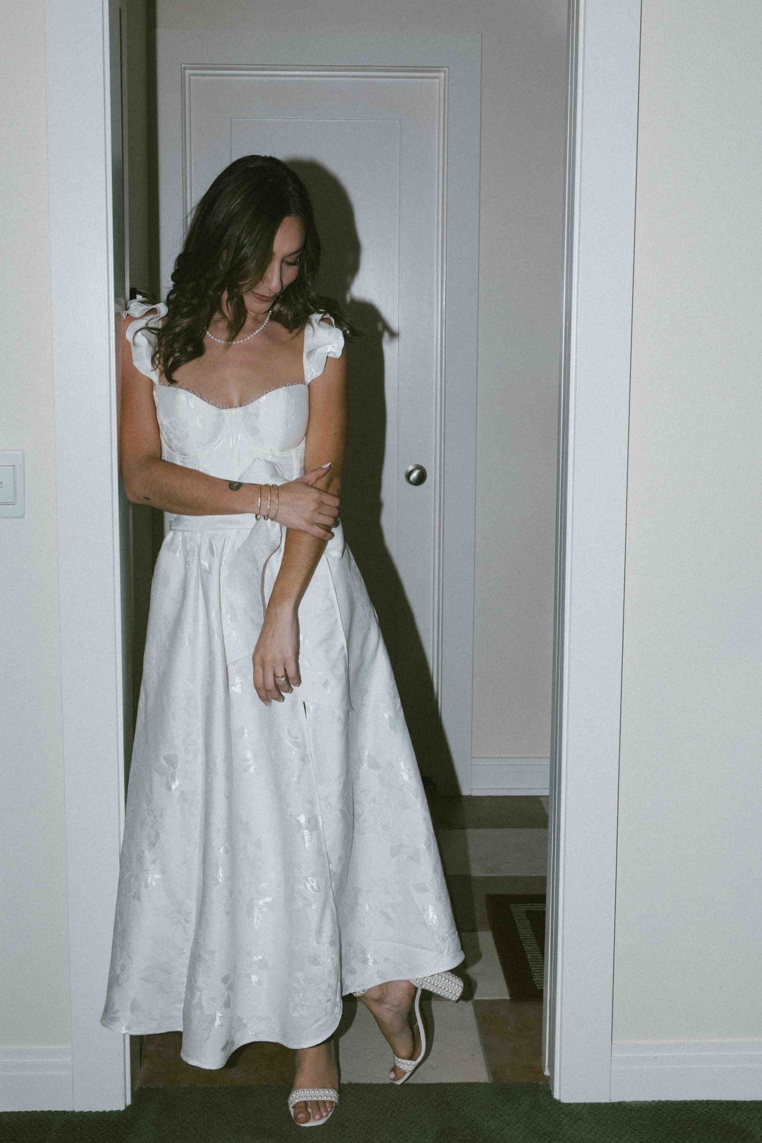 Woman in a white eyelet dress poses in front of a white door showing different angles of the outfit.