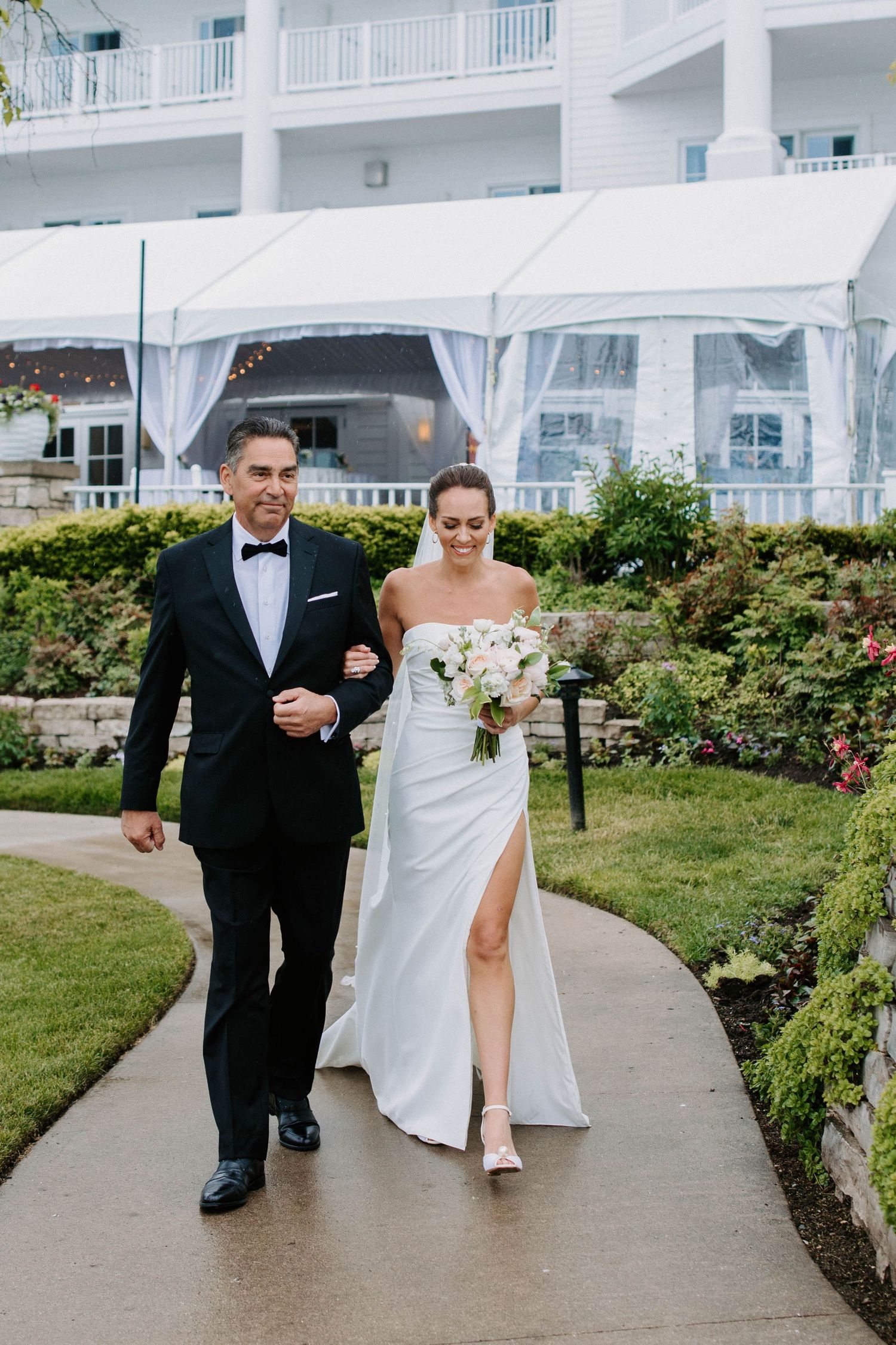 Wedding party walks along curved path with landscaped gardens and white resort building.