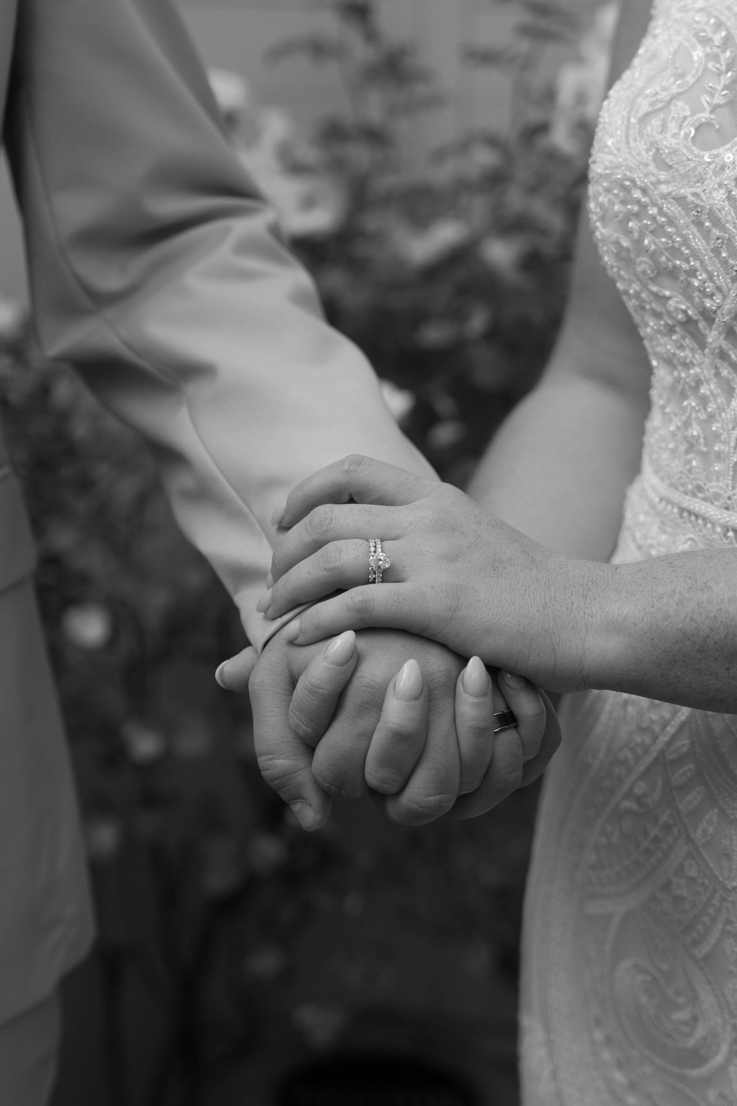 Close-up black and white shot of wedding couple holding hands showing engagement ring detail.