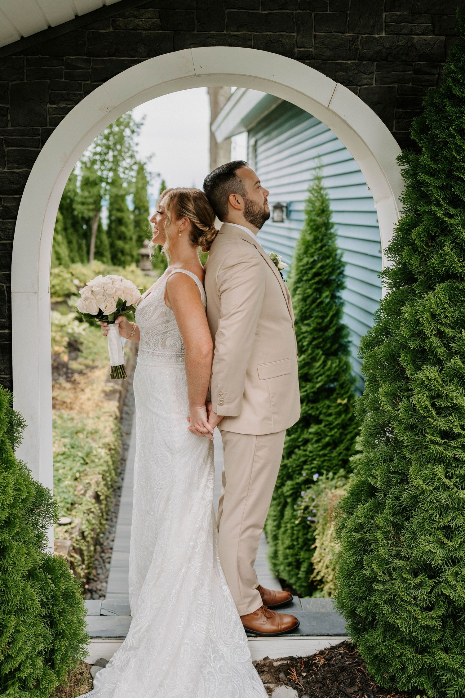 Couple shares intimate wedding moments under white archways surrounded by evergreen trees.