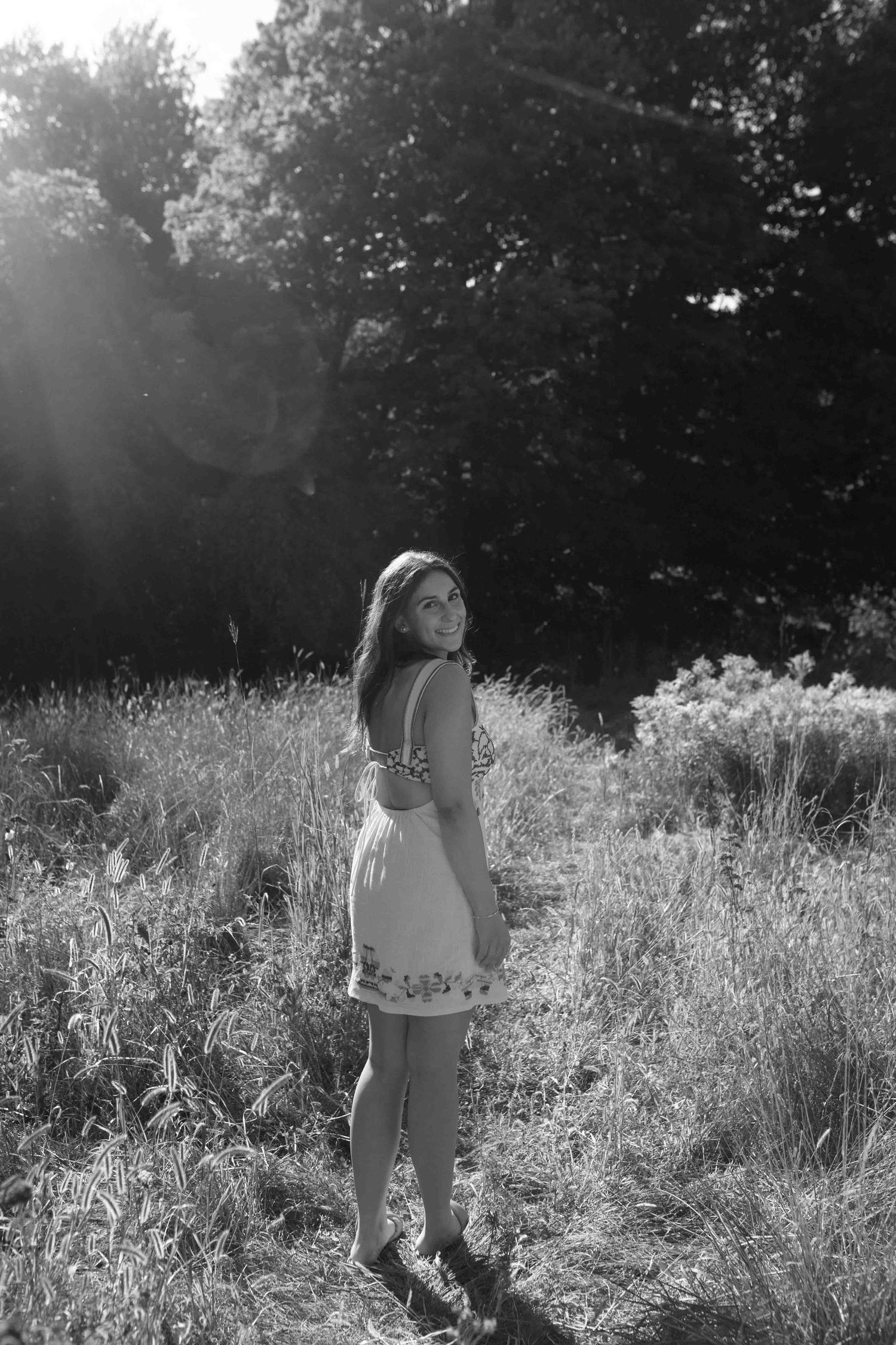 Artistic black and white portrait in a field of tall grass with sunlight filtering through trees.