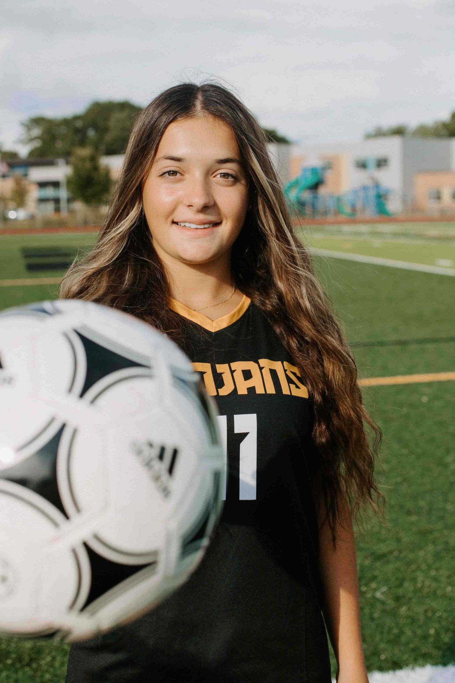 Soccer player poses with soccer balls in Trojans uniform on athletic field.