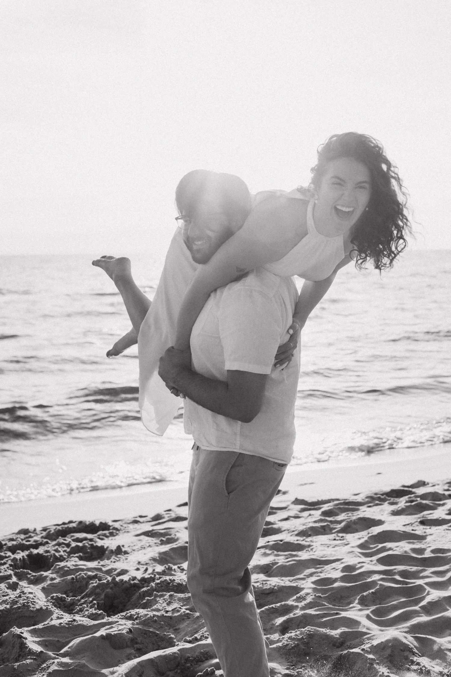 Playful couple embraces on a sunny beach while enjoying a romantic moment.