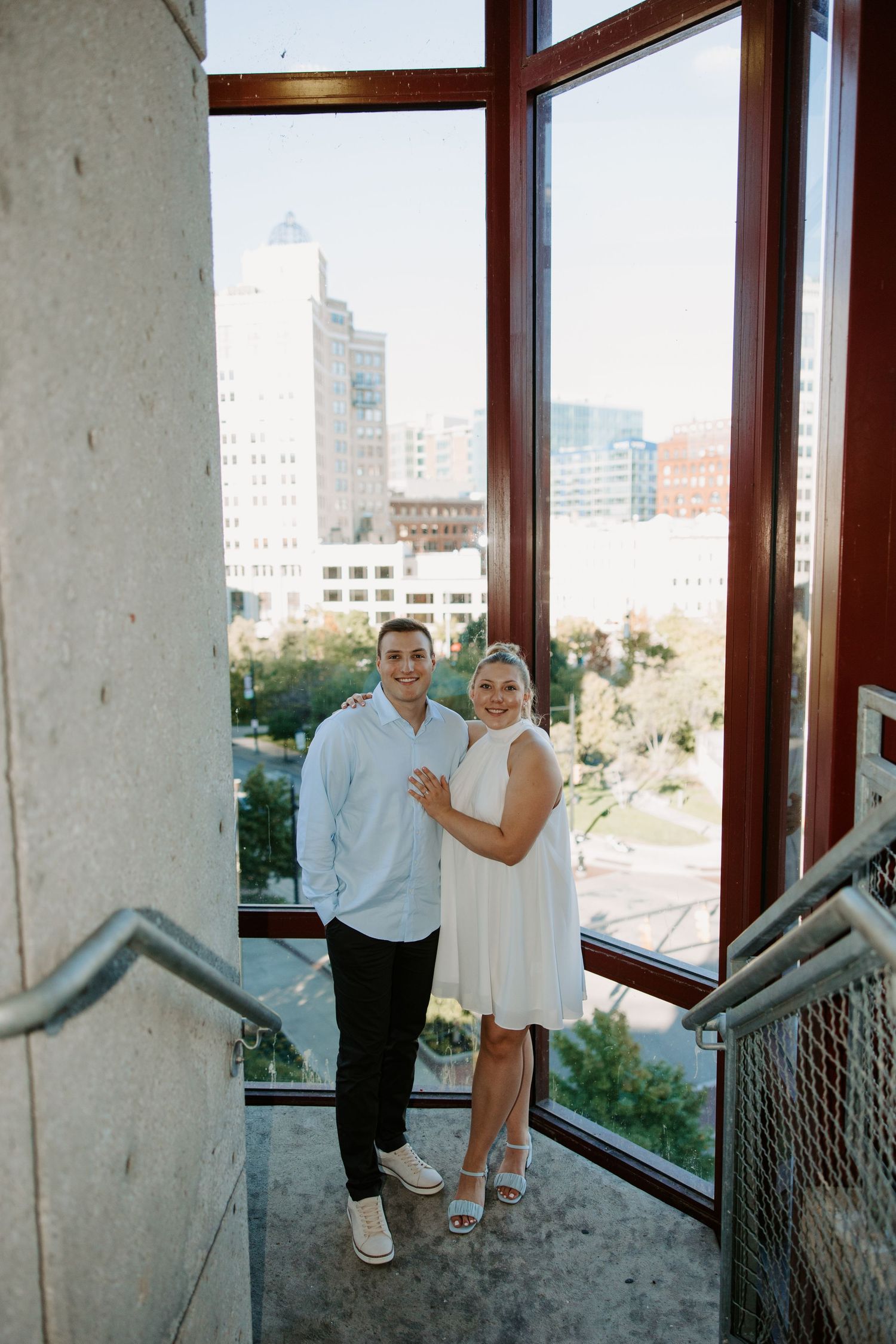 Indoor engagement session in modern building with large windows overlooking cityscape.