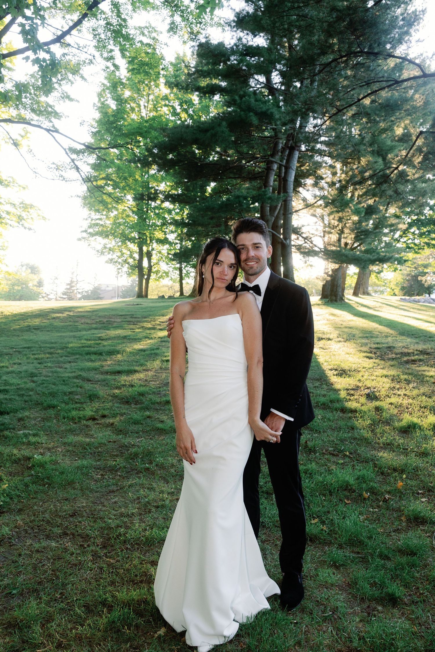 Wedding couple poses for romantic portraits on a grassy hillside at sunset.