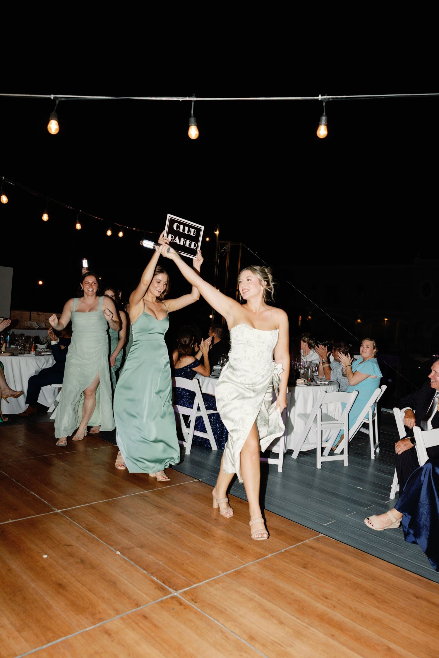 Wedding reception dance floor with guests in mint green dresses celebrating under string lights.