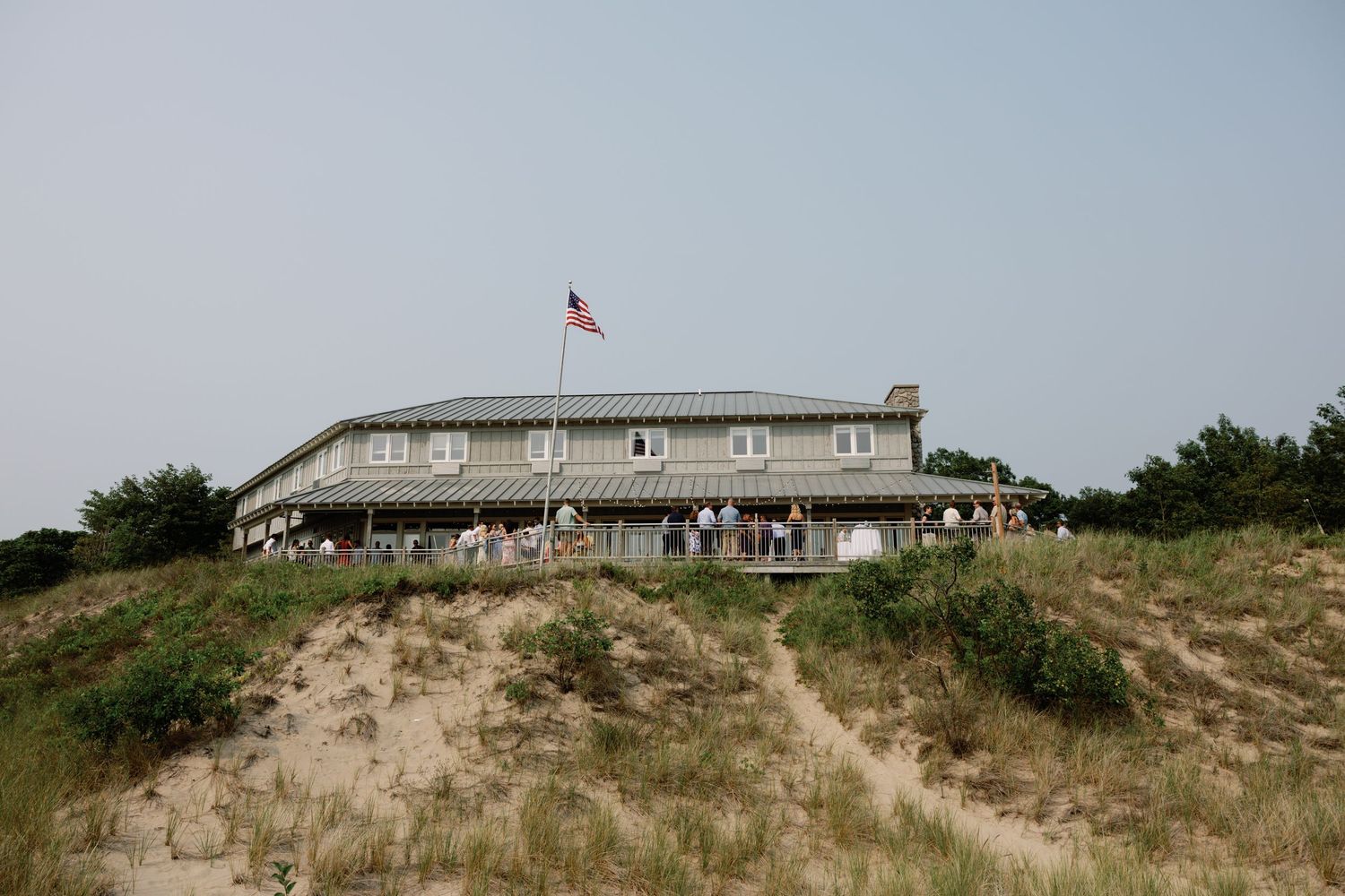 A coastal building sits atop sandy dunes with an American flag flying in the breeze.