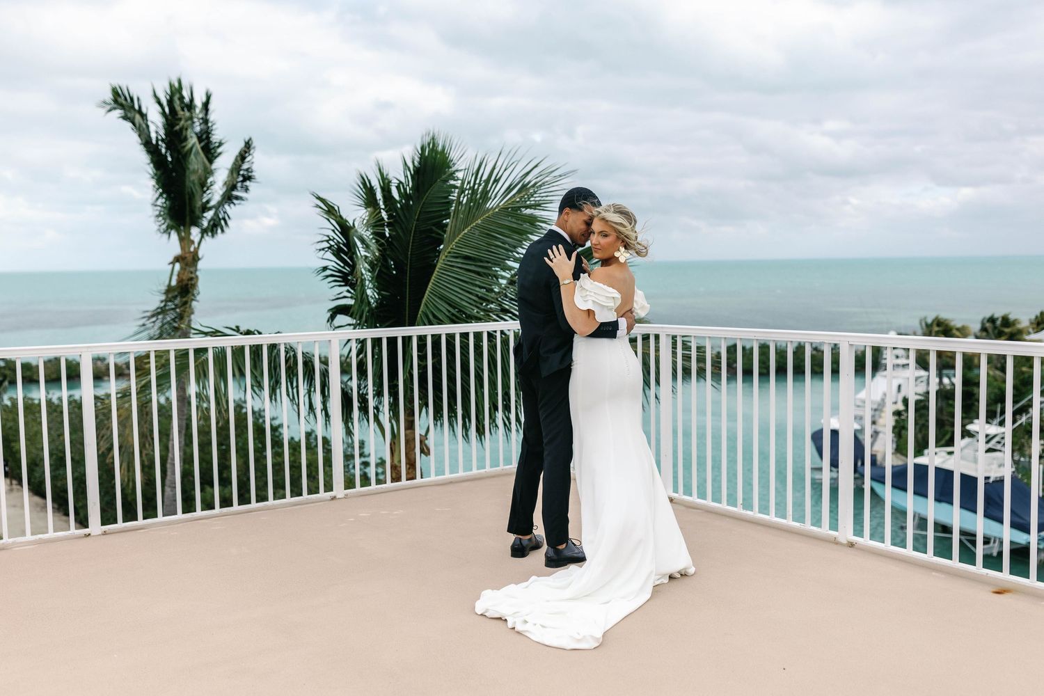 Seaside wedding photos on a white balcony with ocean and palm tree views.