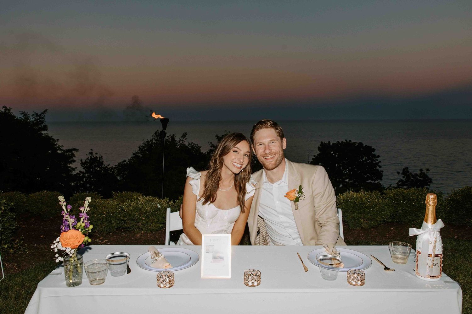 An elegant outdoor wedding reception setup with ocean views at dusk.