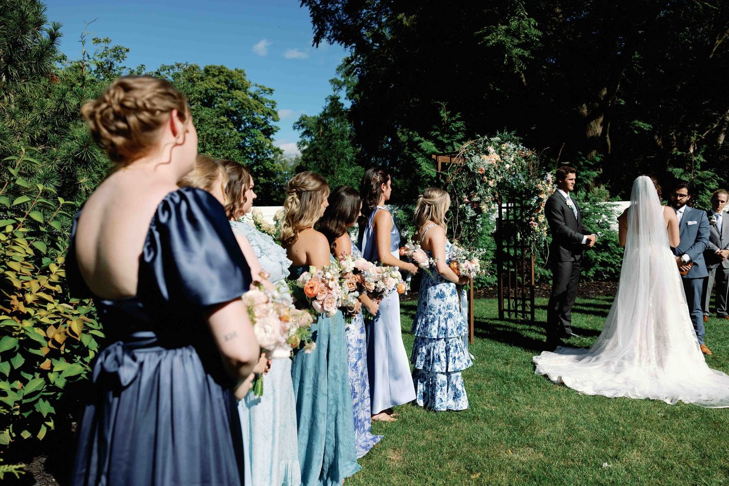 Wedding party and guests gathered outdoors with bridesmaids in blue dresses.