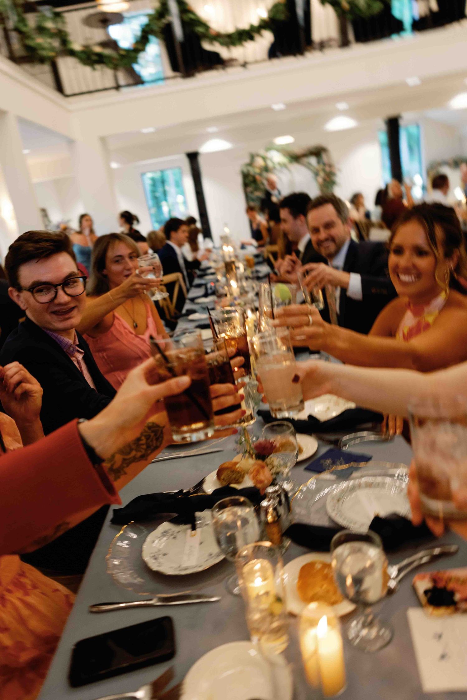 Wedding guests enjoying dinner and toasting at reception tables with candlelight.