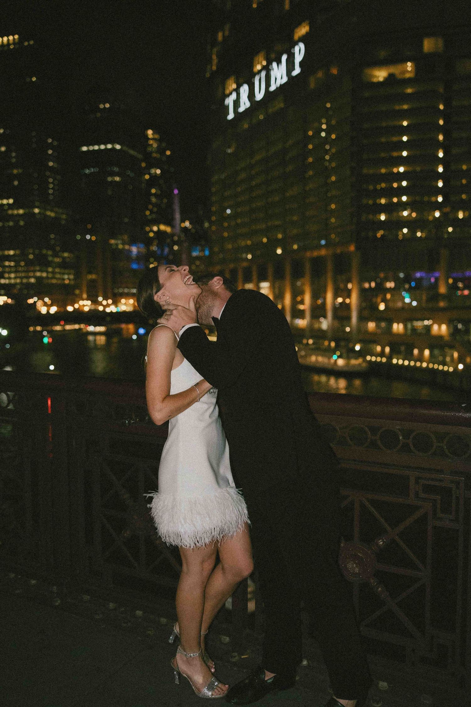 Romantic nighttime moment on a bridge with city lights glowing in the background.
