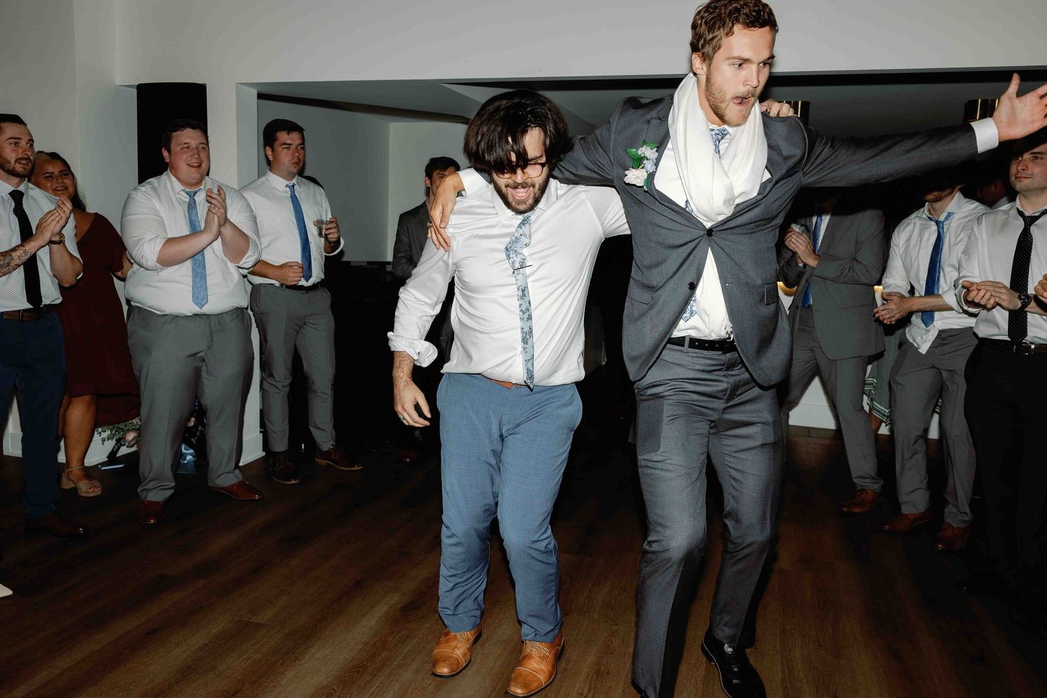 Groomsmen in grey suits dancing energetically at a wedding reception.