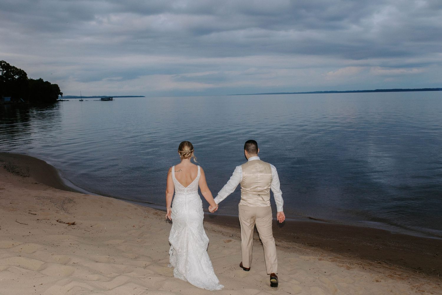 A couple walks along the shoreline with dramatic cloudy skies and calm waters.