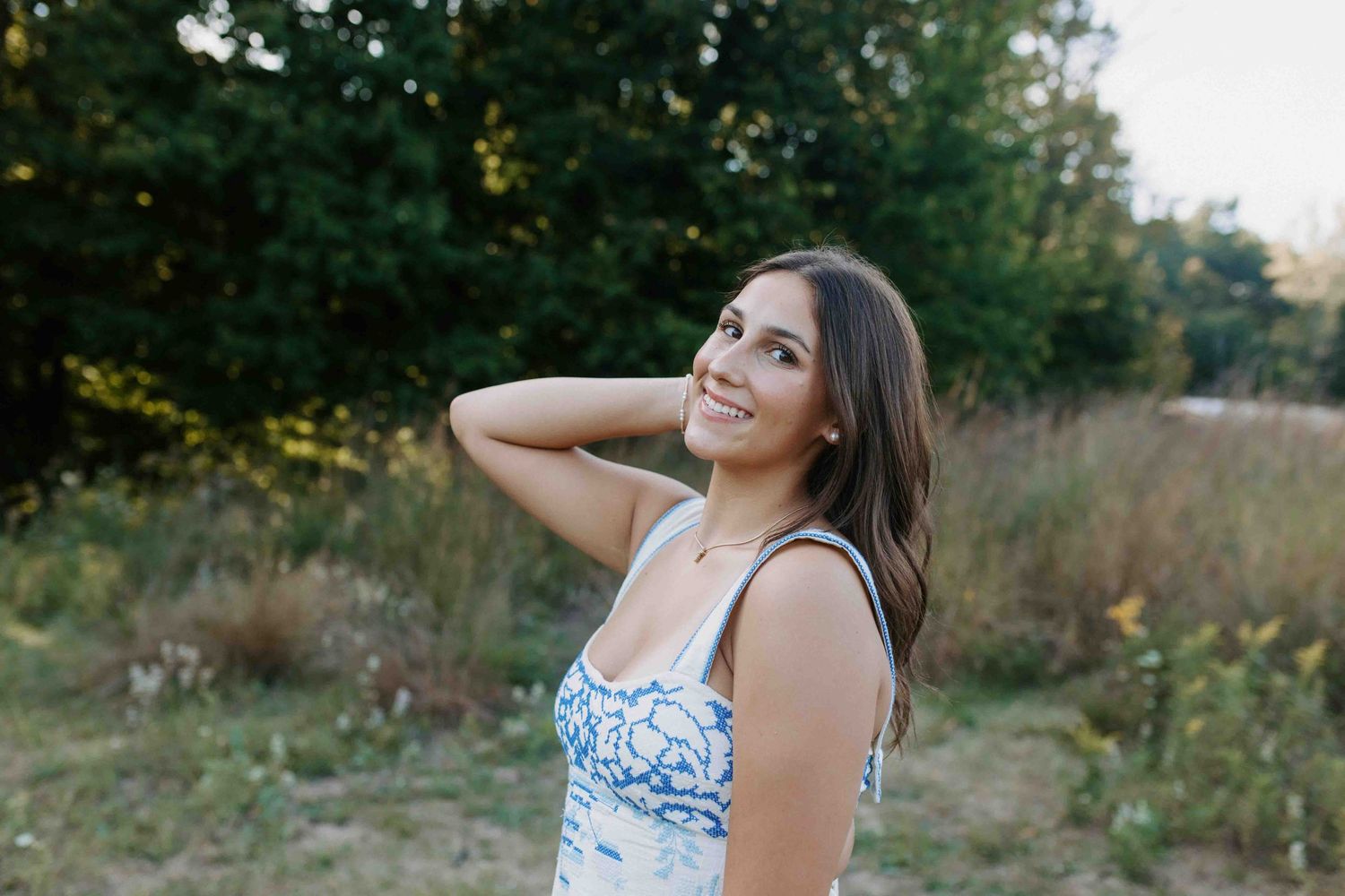 Candid summer portrait in white dress against golden hour lighting and natural backdrop.