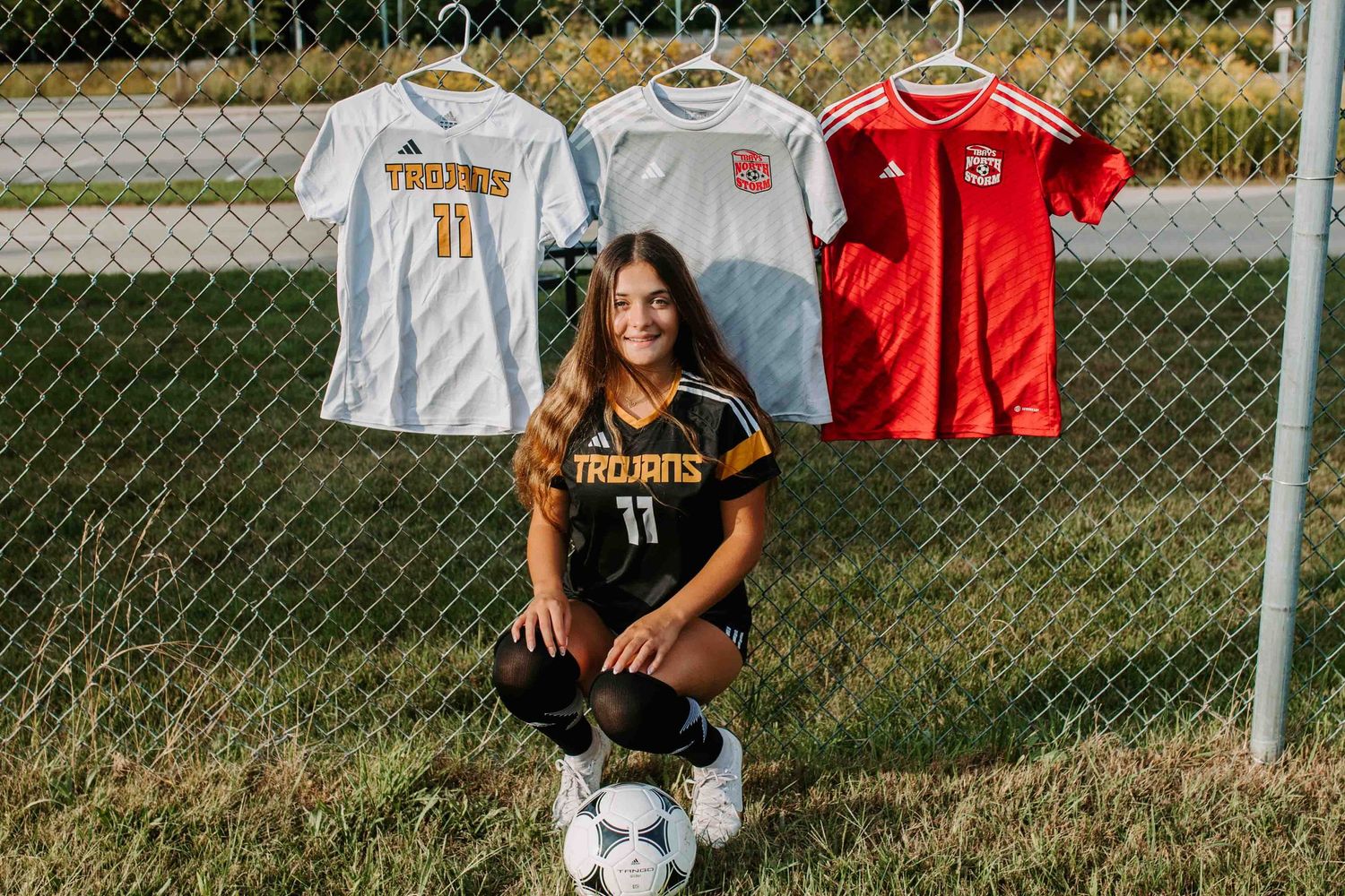Soccer jerseys hanging on chain link fence with player and ball.