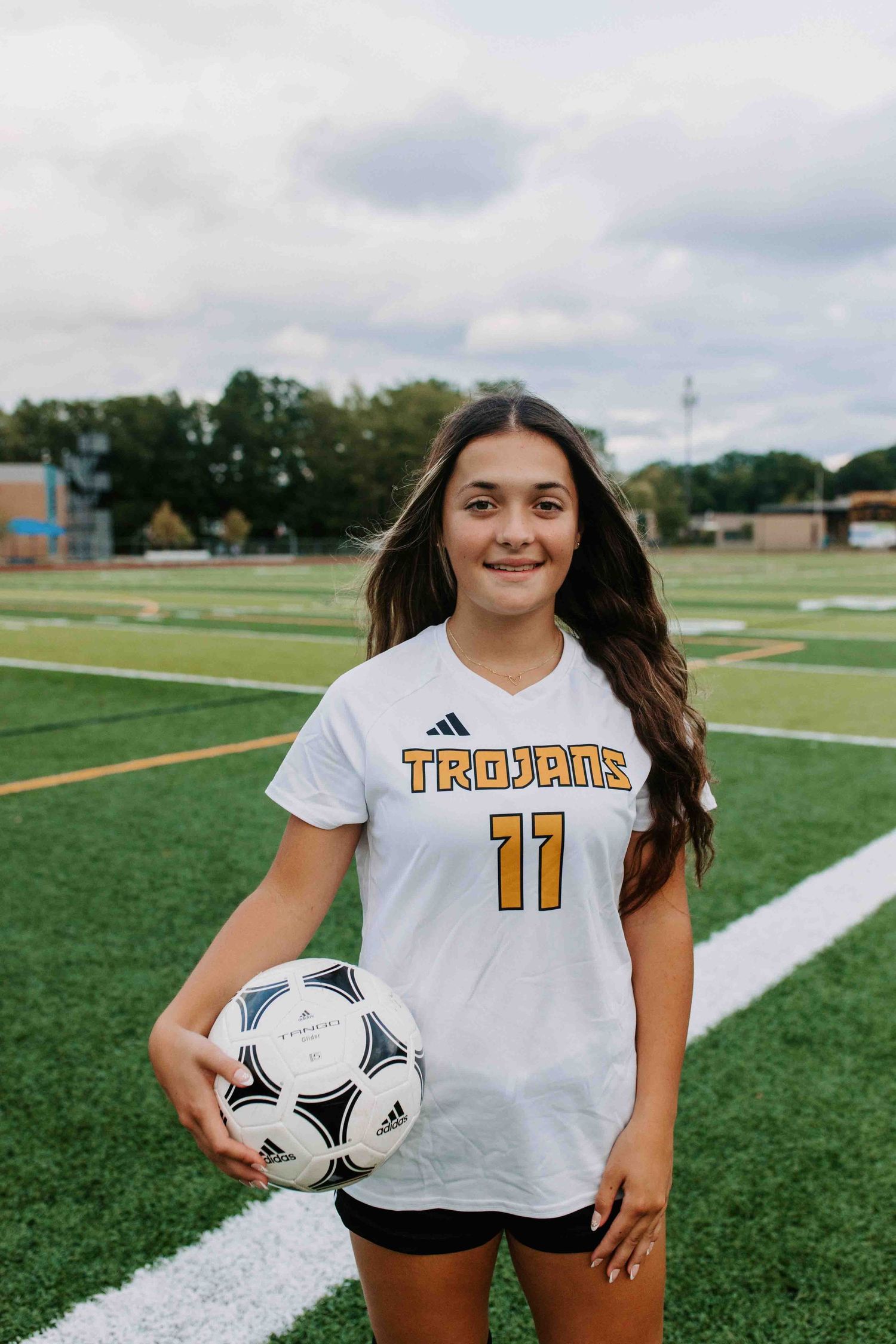 Soccer player wearing white Trailblazers jersey number 11 poses with ball on sports field.