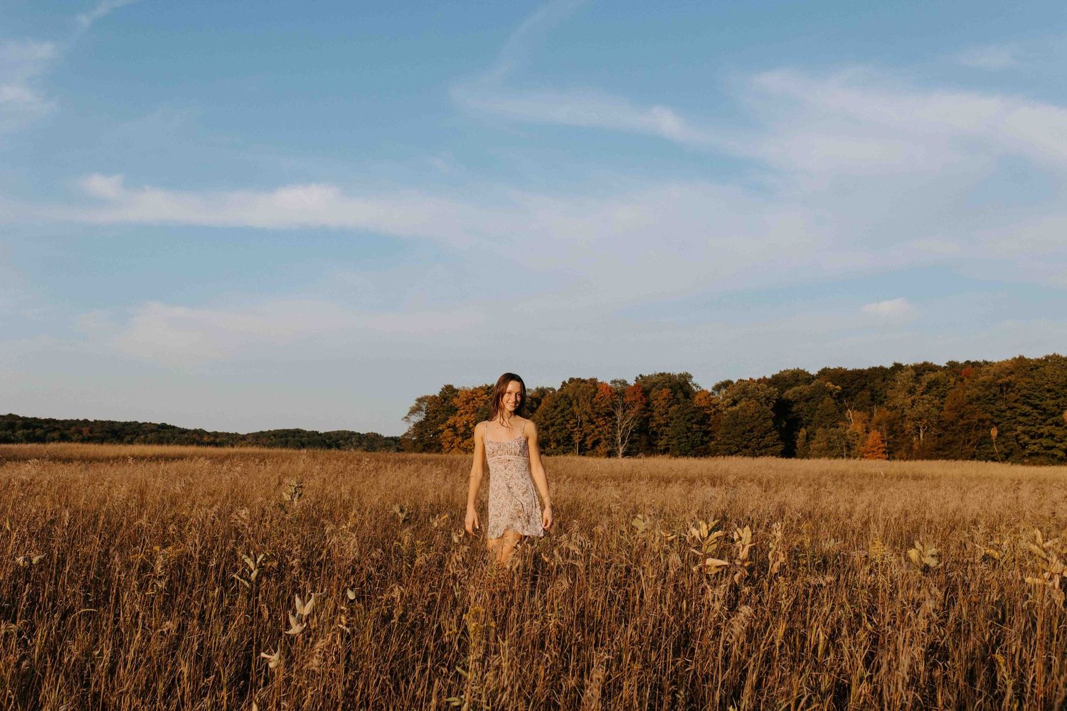 Wide landscape shot of a figure in a white dress standing in a vast autumn field.