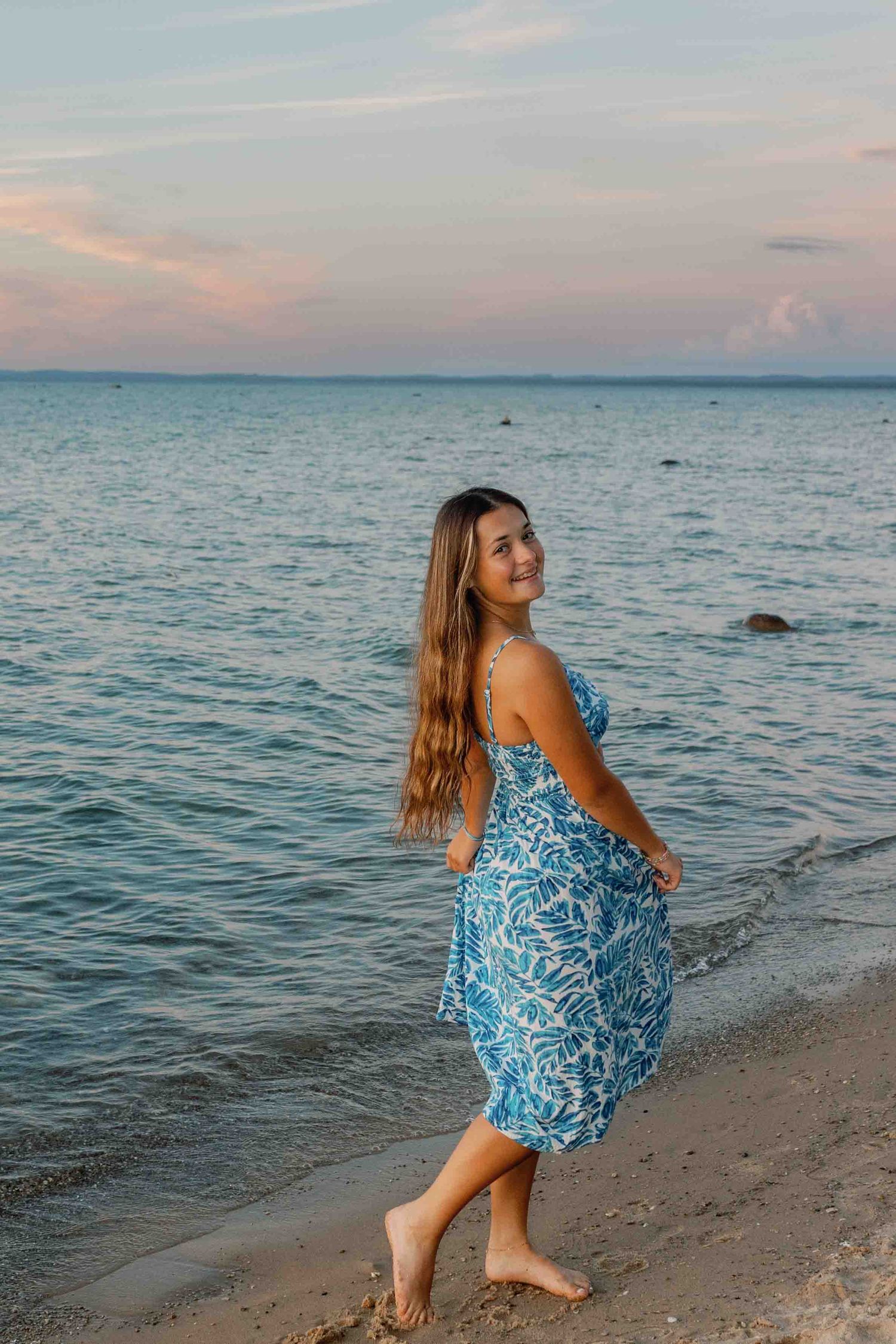 Dancing along the shoreline in a blue and white printed dress as waves gently lap at the beach.