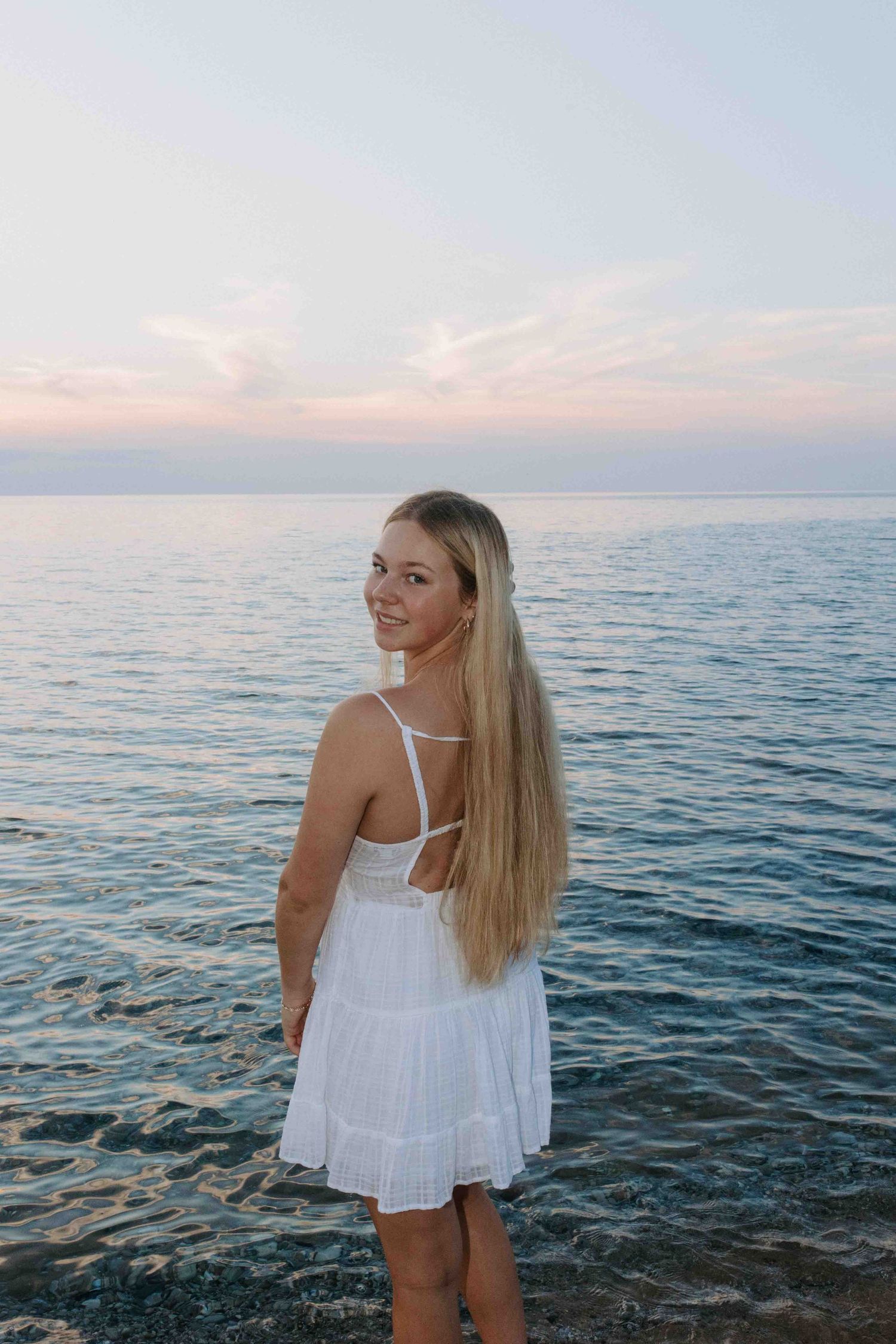 Candid seaside moments captured with the subject wearing a white ruffled dress against blue waters.