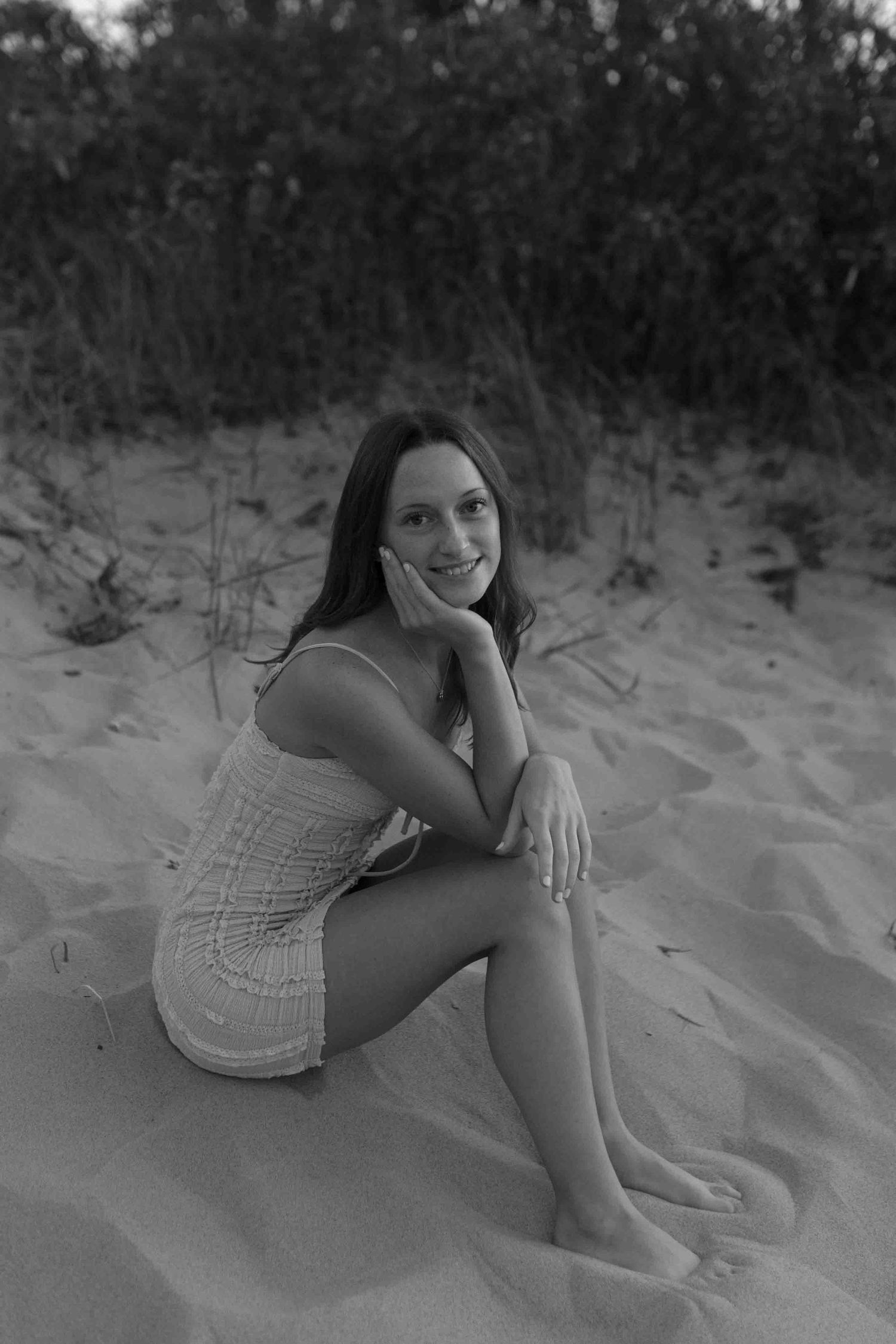Black and white portrait of someone reclining on sandy beach dunes.