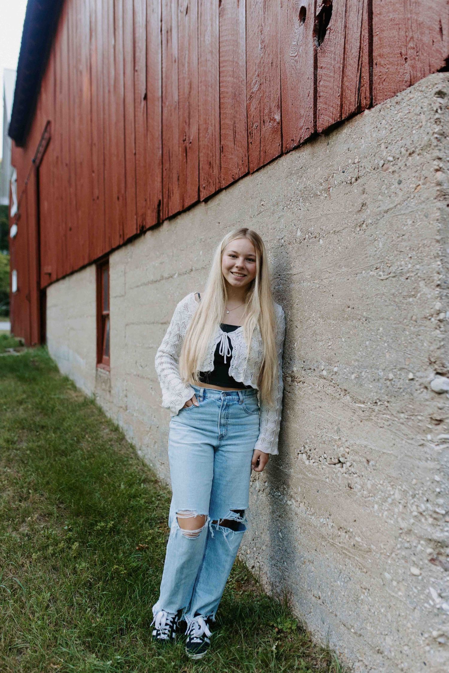 Casual poses against a rustic red barn wall showing distressed denim and knit sweater style.