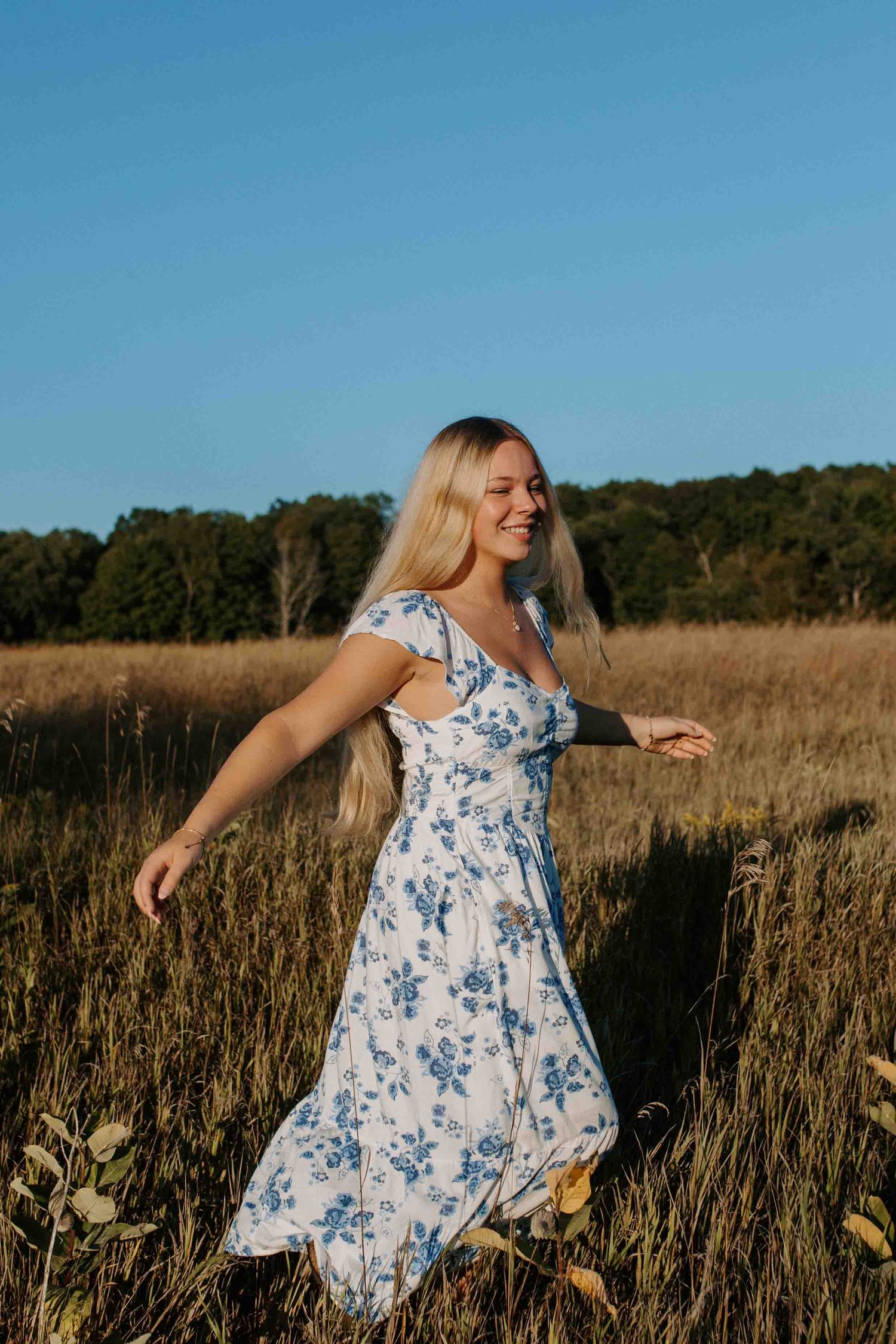 A blue and white floral dress flows in a golden field during sunset.