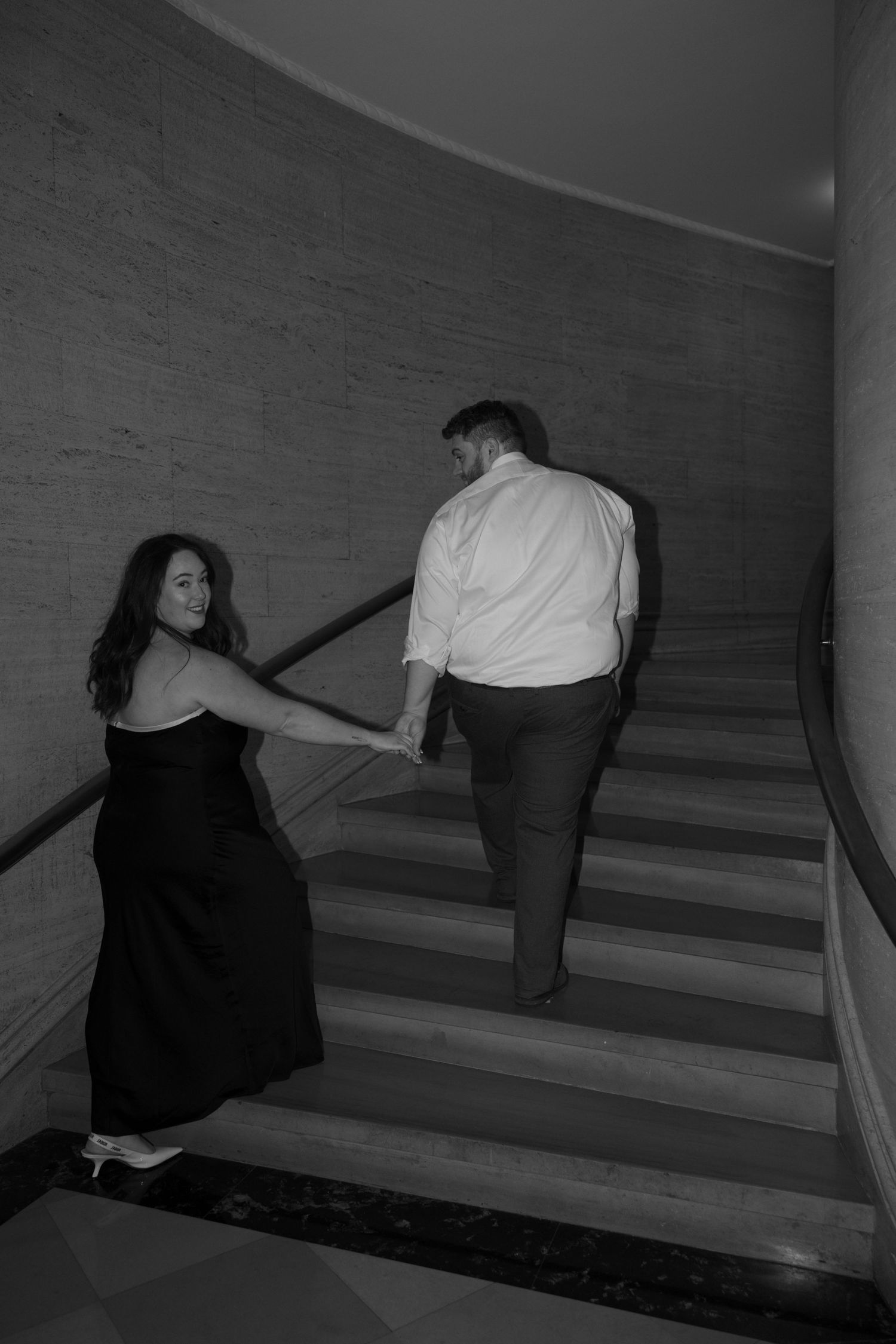 A couple descends a dimly lit staircase in a moody black and white composition.