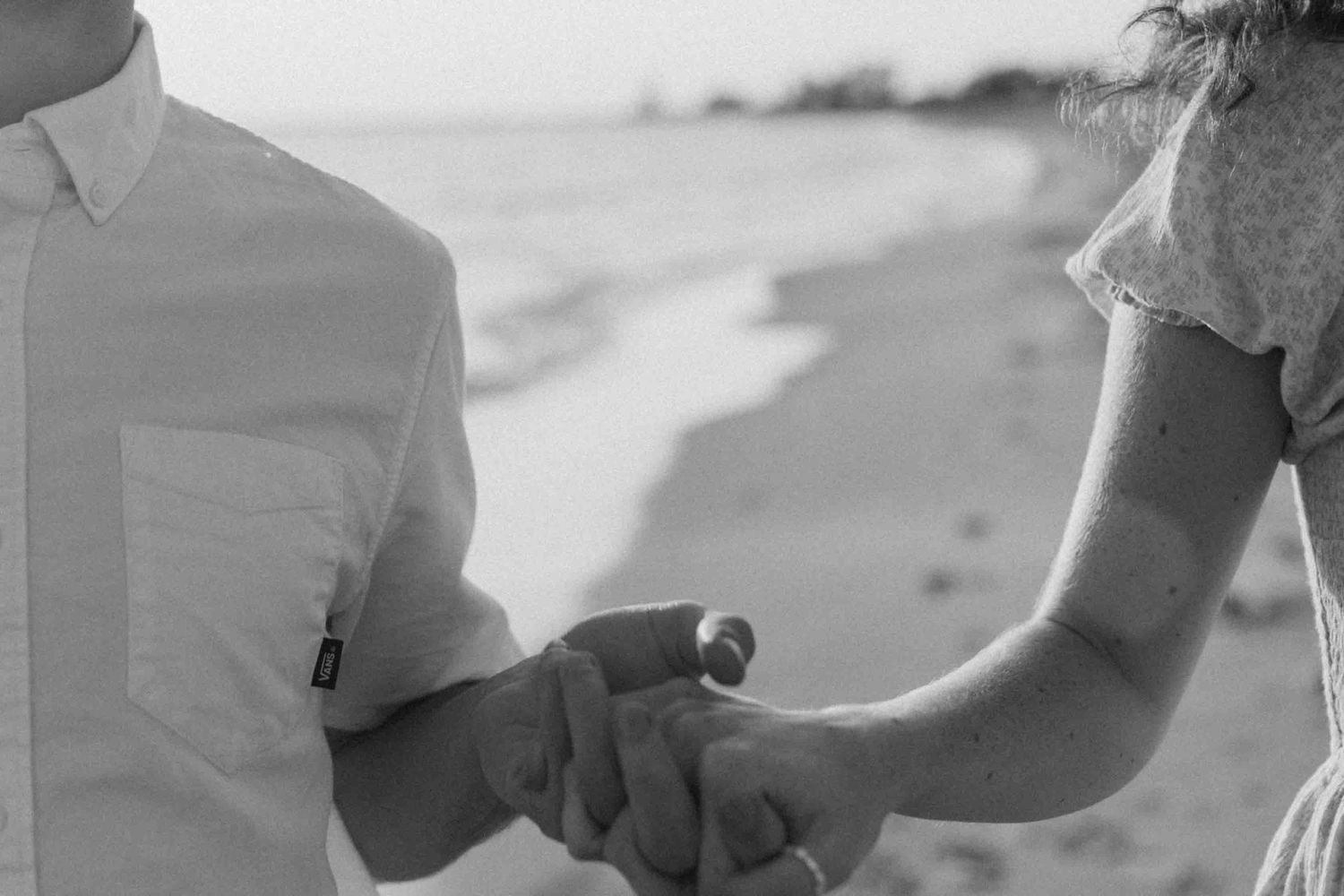A couple in white clothing shares a tender moment on a beach during sunset.