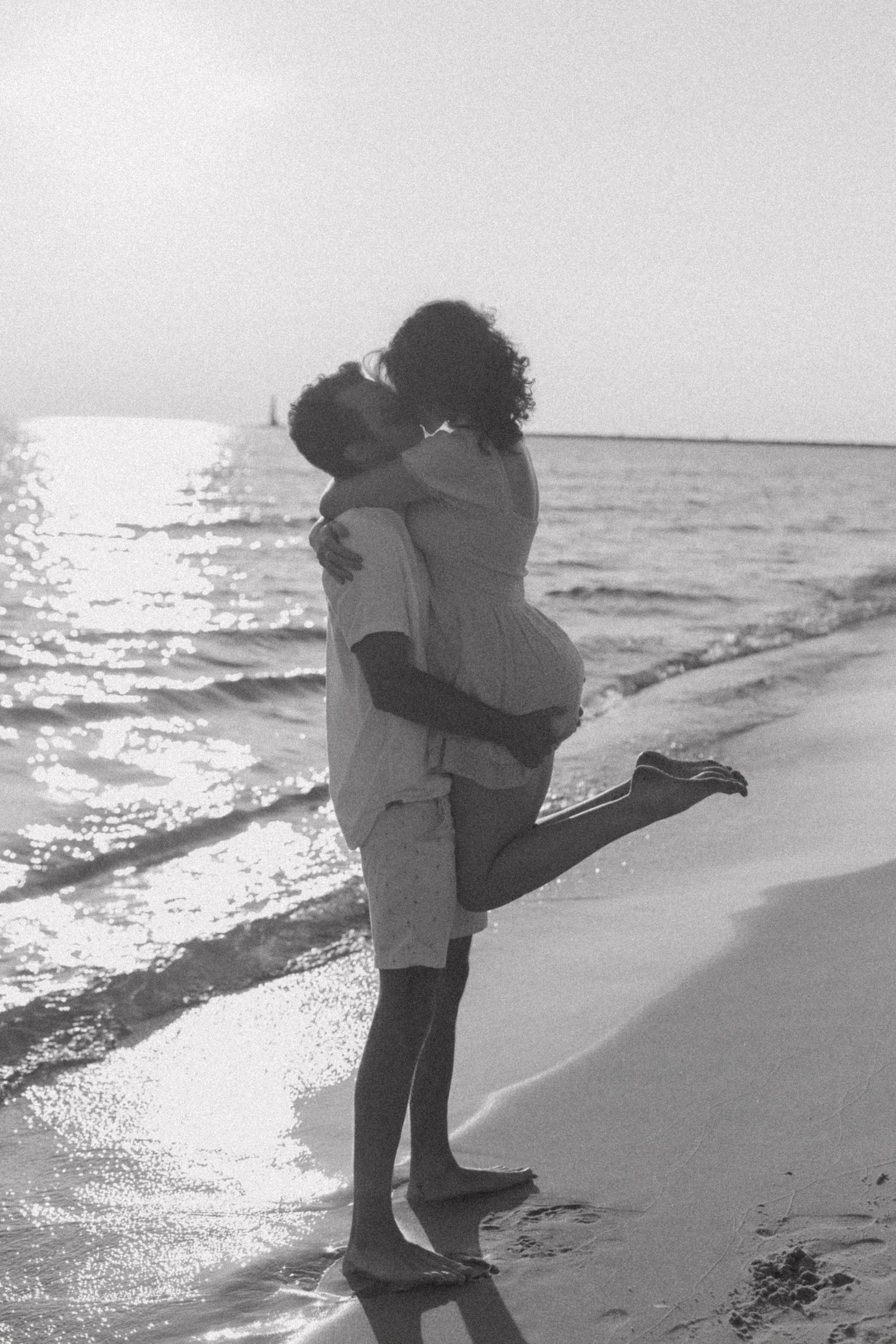 Couple embracing on a scenic beach shoreline in black and white.