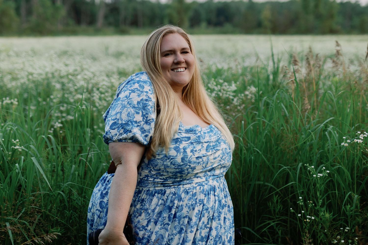 Woman in blue floral dress poses in a sunny wildflower field.