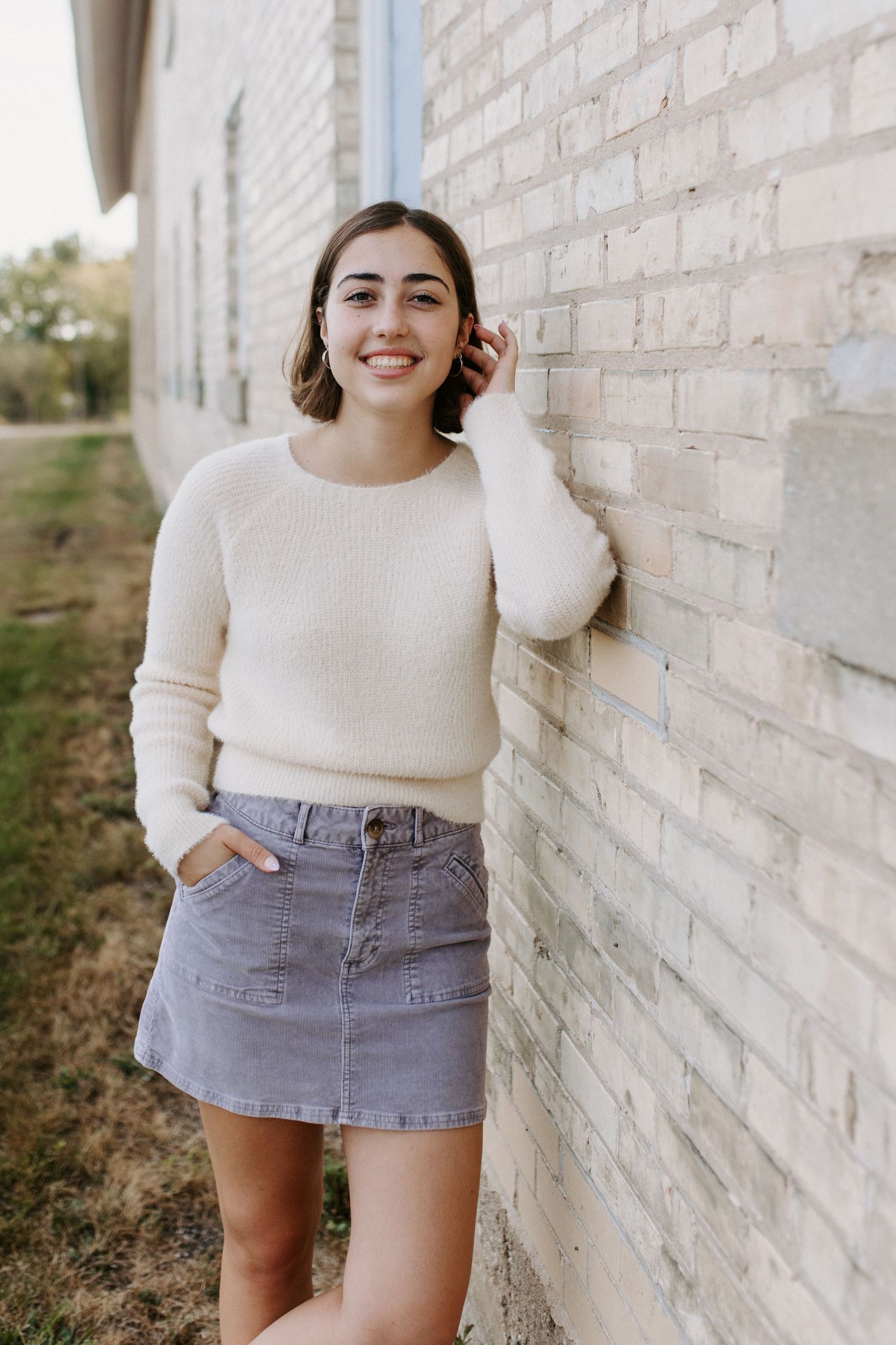 Cream sweater and gray denim mini skirt styled against white brick wall in outdoor photoshoot.
