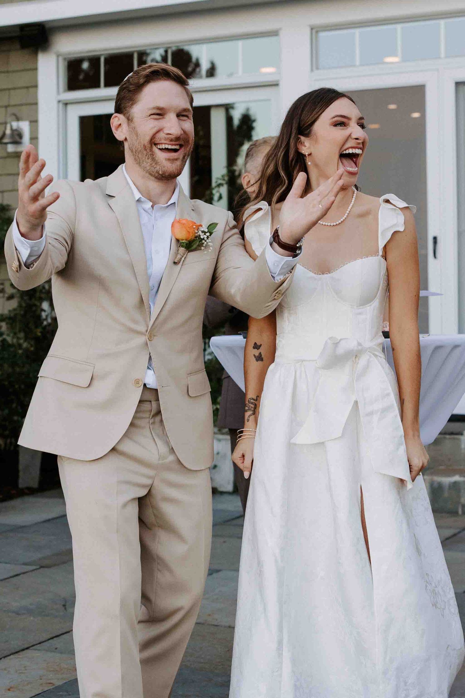 Joyful couple laughing together outside building in wedding attire.