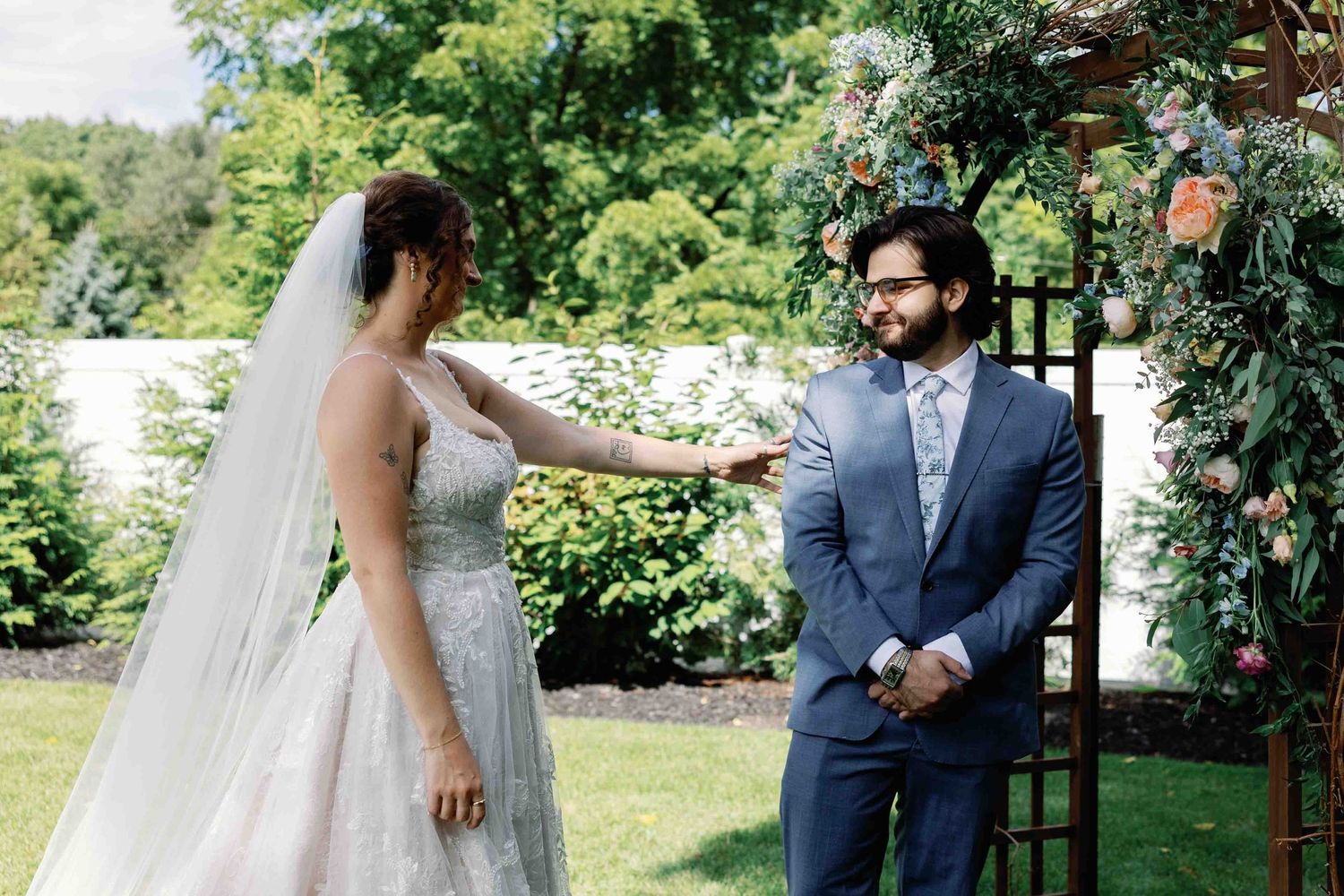 A romantic outdoor wedding ceremony with bridesmaids in light blue dresses gathered on a lush green lawn.