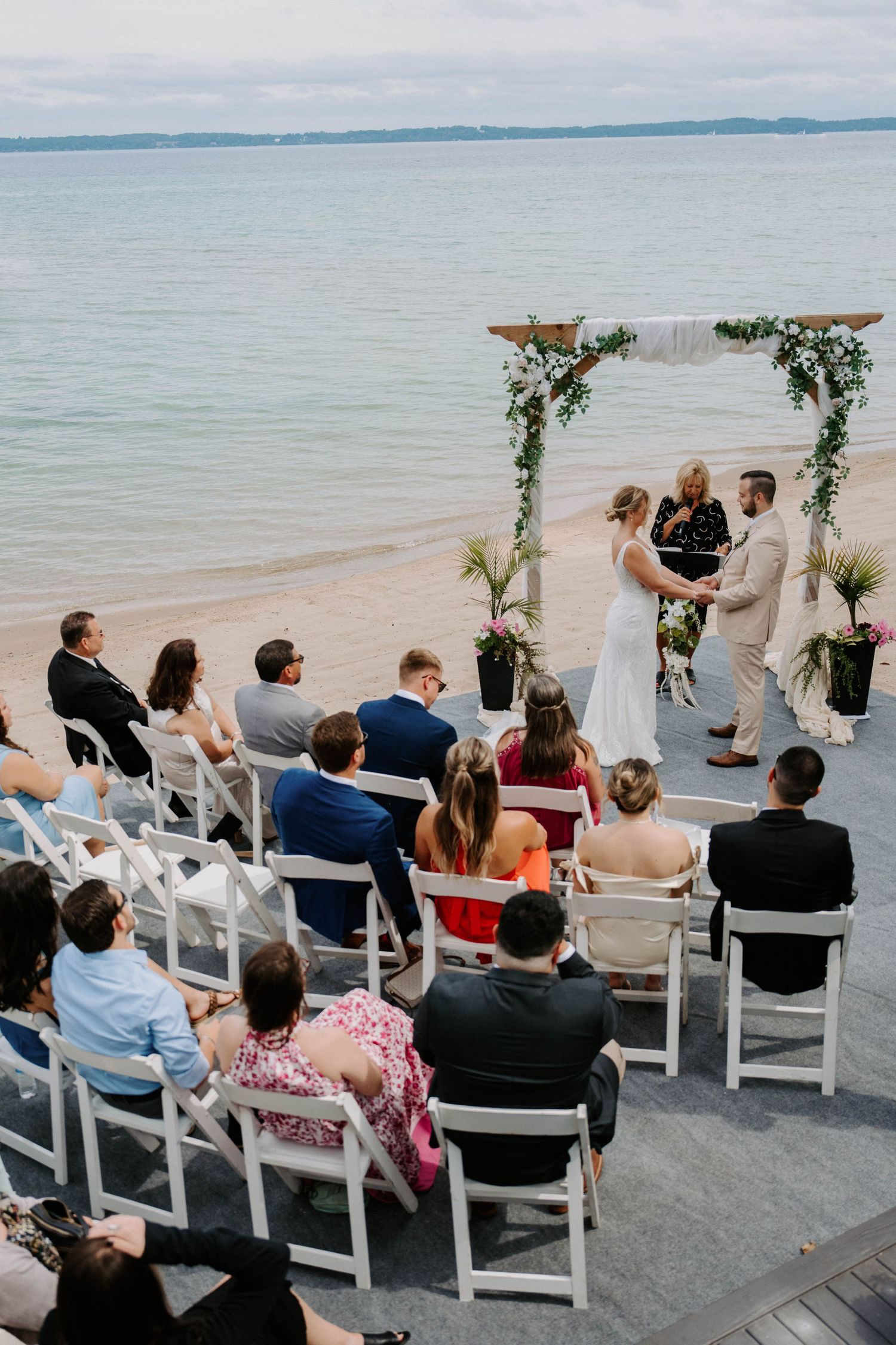 Beachfront wedding ceremony with white chairs and floral arch overlooking the ocean.