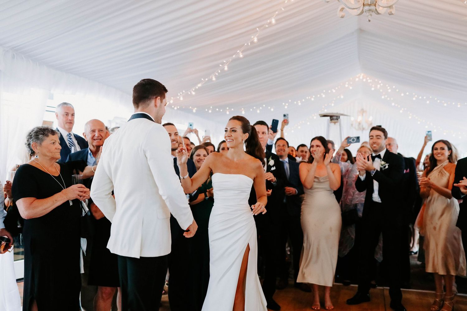 Wedding party dancing and celebrating in a white tent reception space.