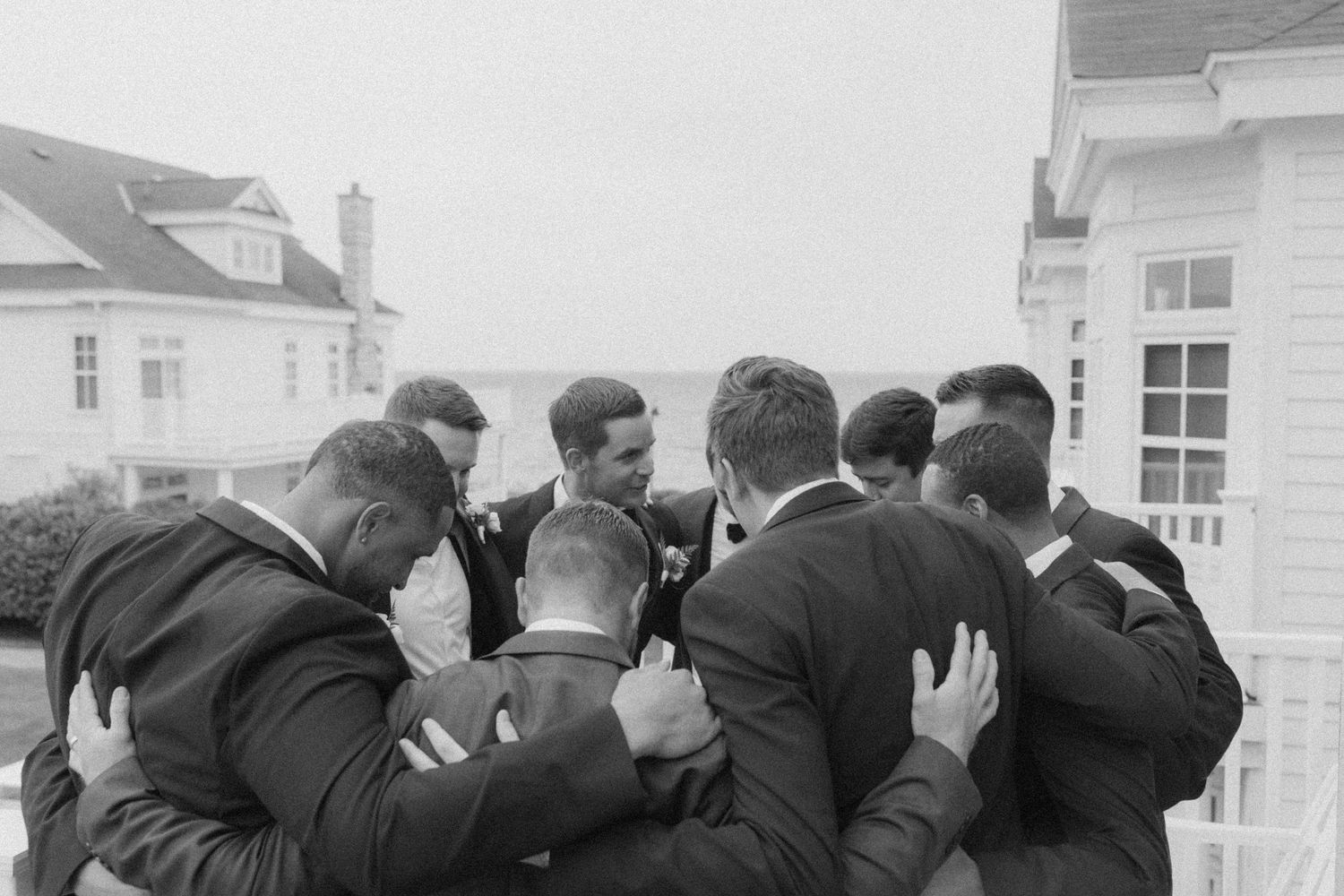 Wedding party in formal attire gathered on a seaside porch.