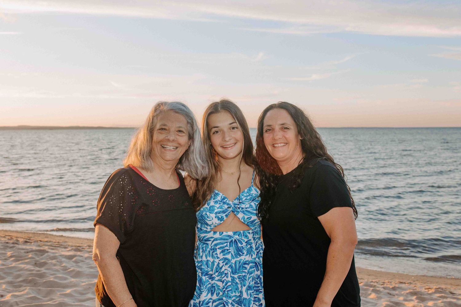 Three people pose together on a beach at sunset with the ocean in the background.