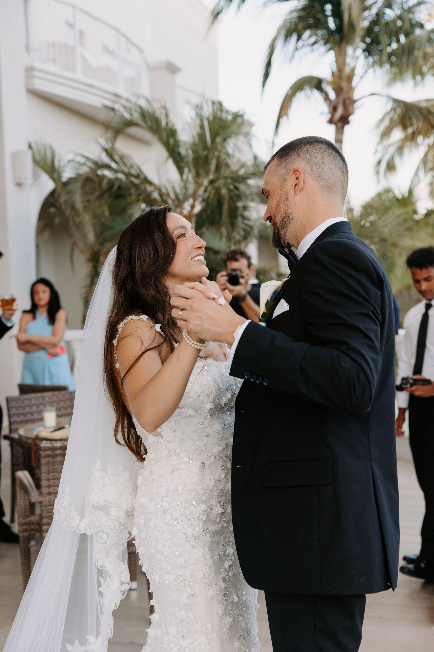 Newlyweds share a romantic first dance on a palm-lined patio at their tropical wedding reception.